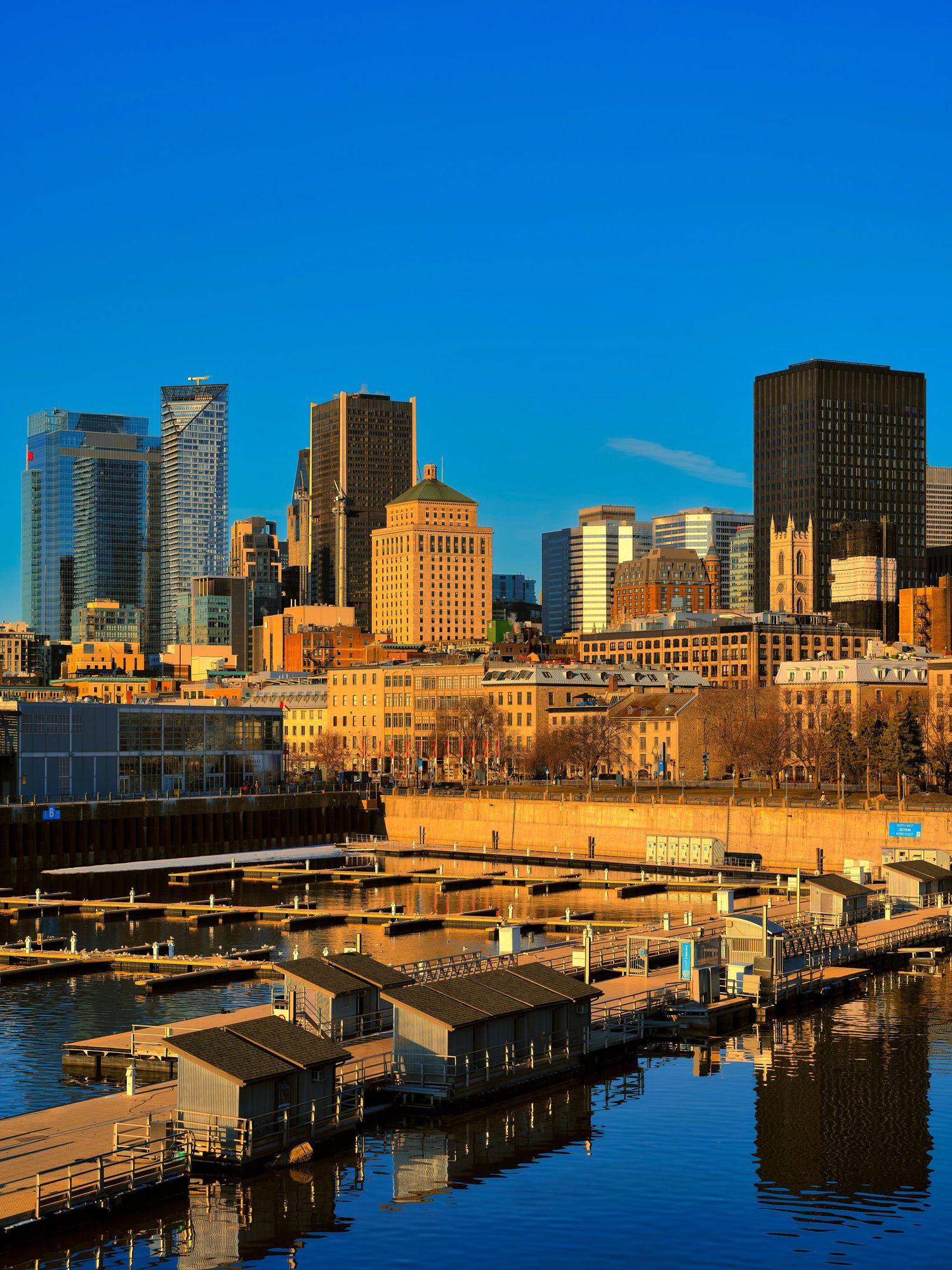 Panoramic view of Montreal's downtown skyline and harbor with boats docked along the waterfront at sunset.