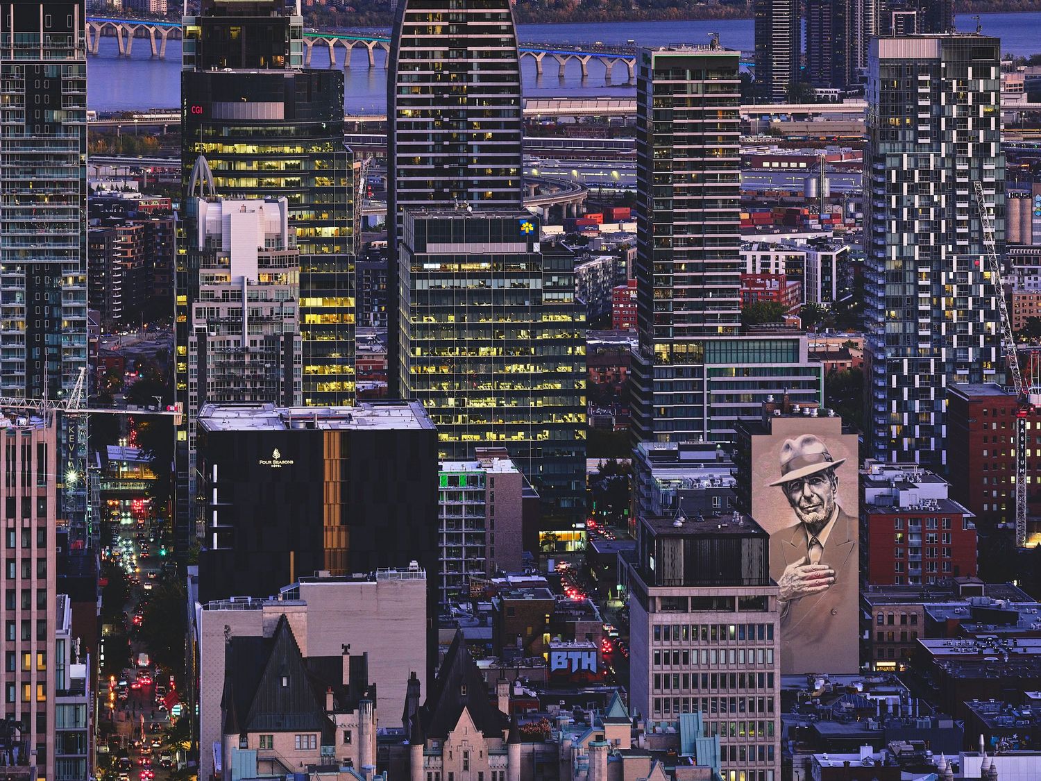Illuminated skyscrapers and office buildings create a dense urban cityscape at twilight with glowing windows and lights.