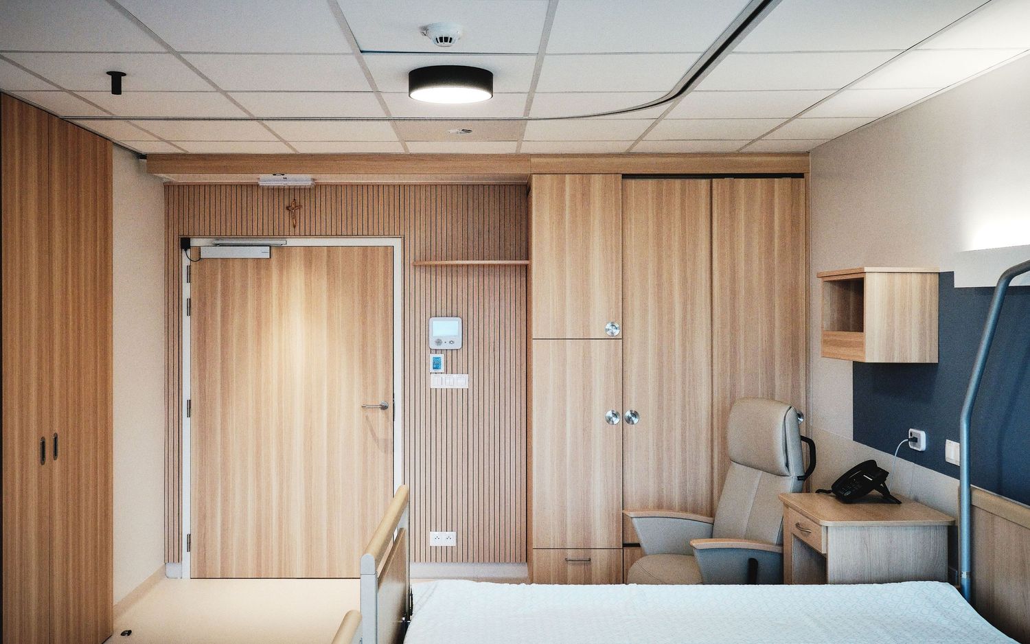 Hospital room interior with wood paneling and medical equipment mounted on walls.