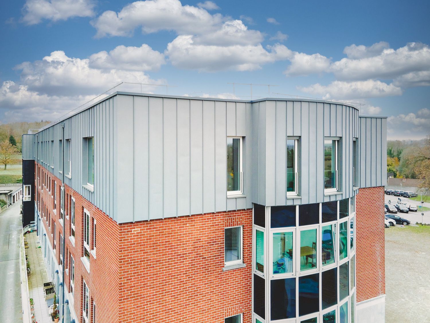 Modern building exterior with metal cladding, red brick base, and curved glass windows.