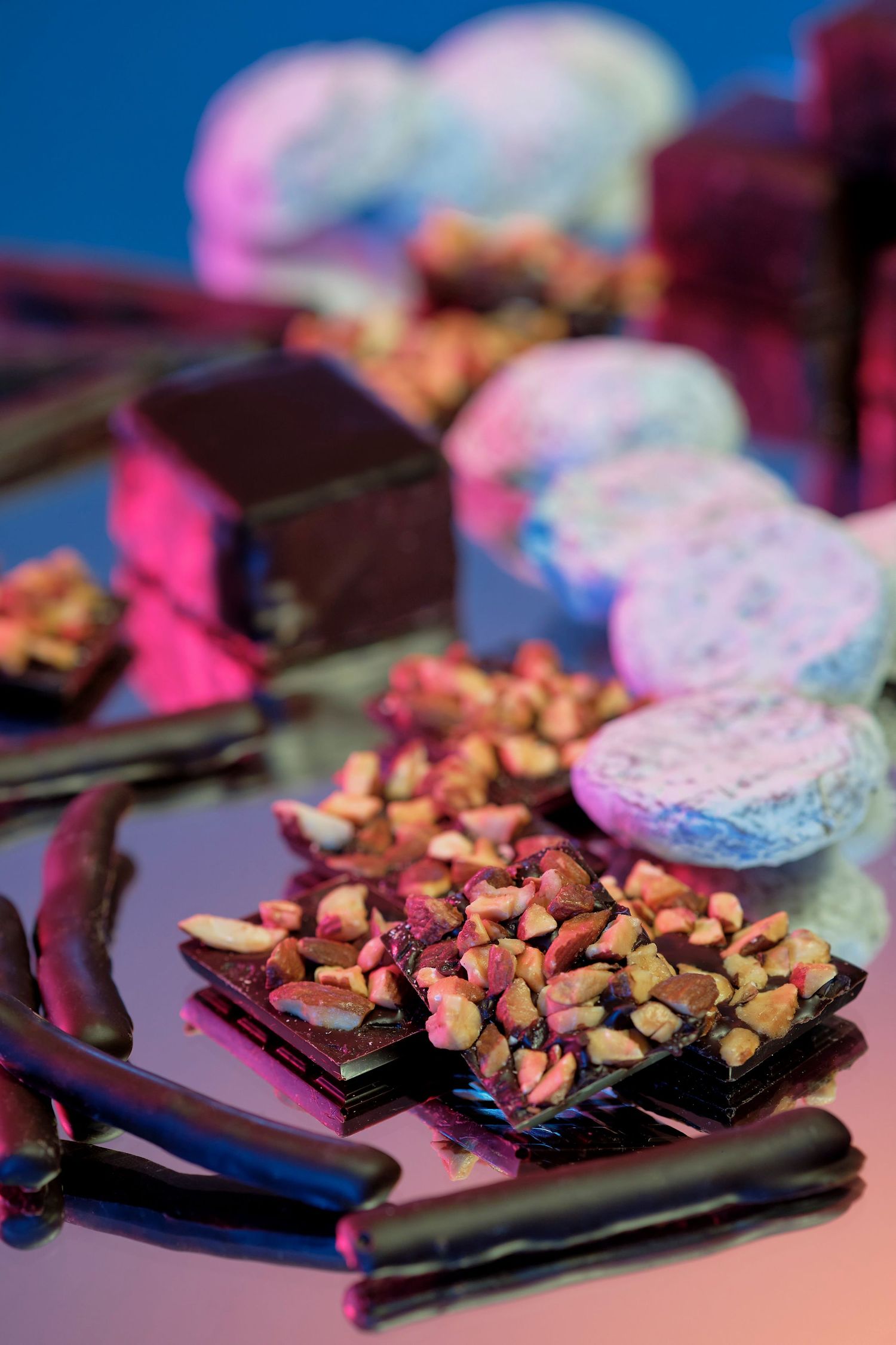 Dark chocolate bars topped with crushed nuts on a blue background with pink lighting.