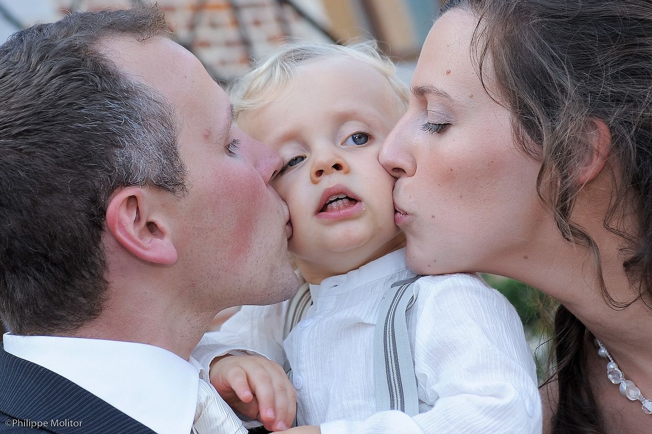 Parents lovingly kiss their young toddler son on both cheeks simultaneously.