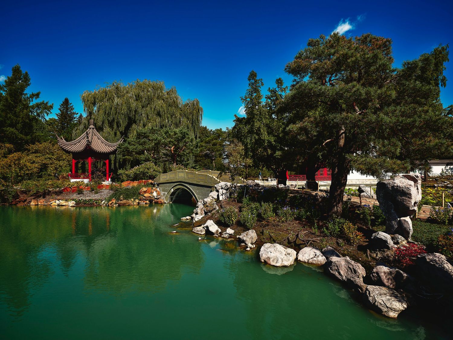 Serene Chinese garden with pagodas and stone bridges reflected in a tranquil pond.