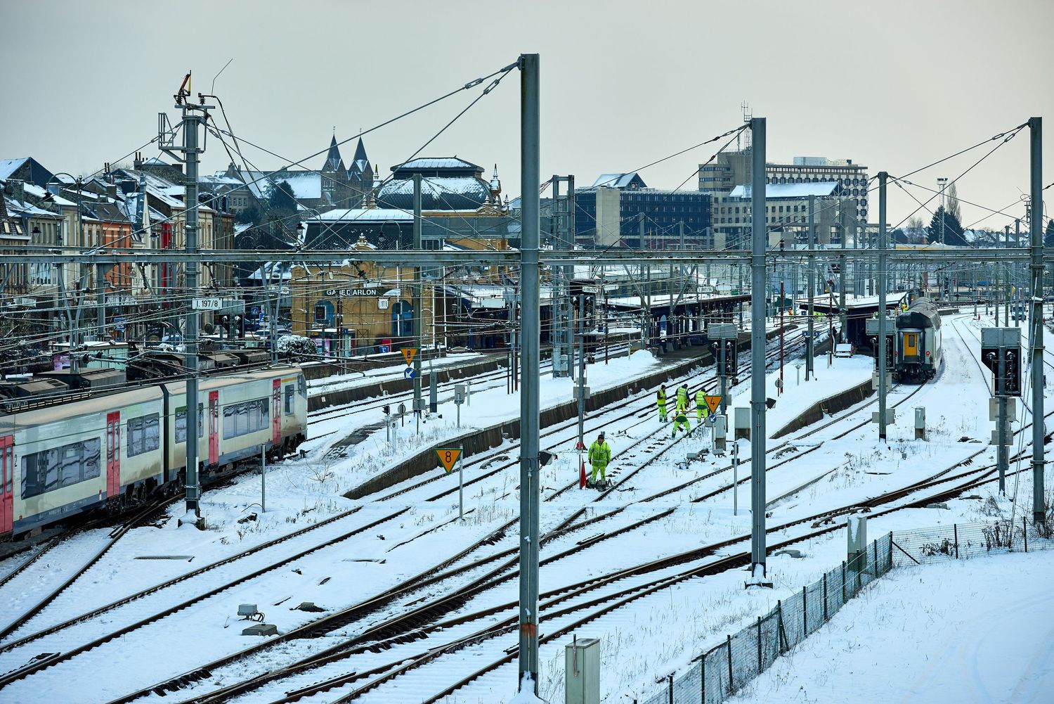 Snow covered railway tracks and infrastructure in an urban setting.