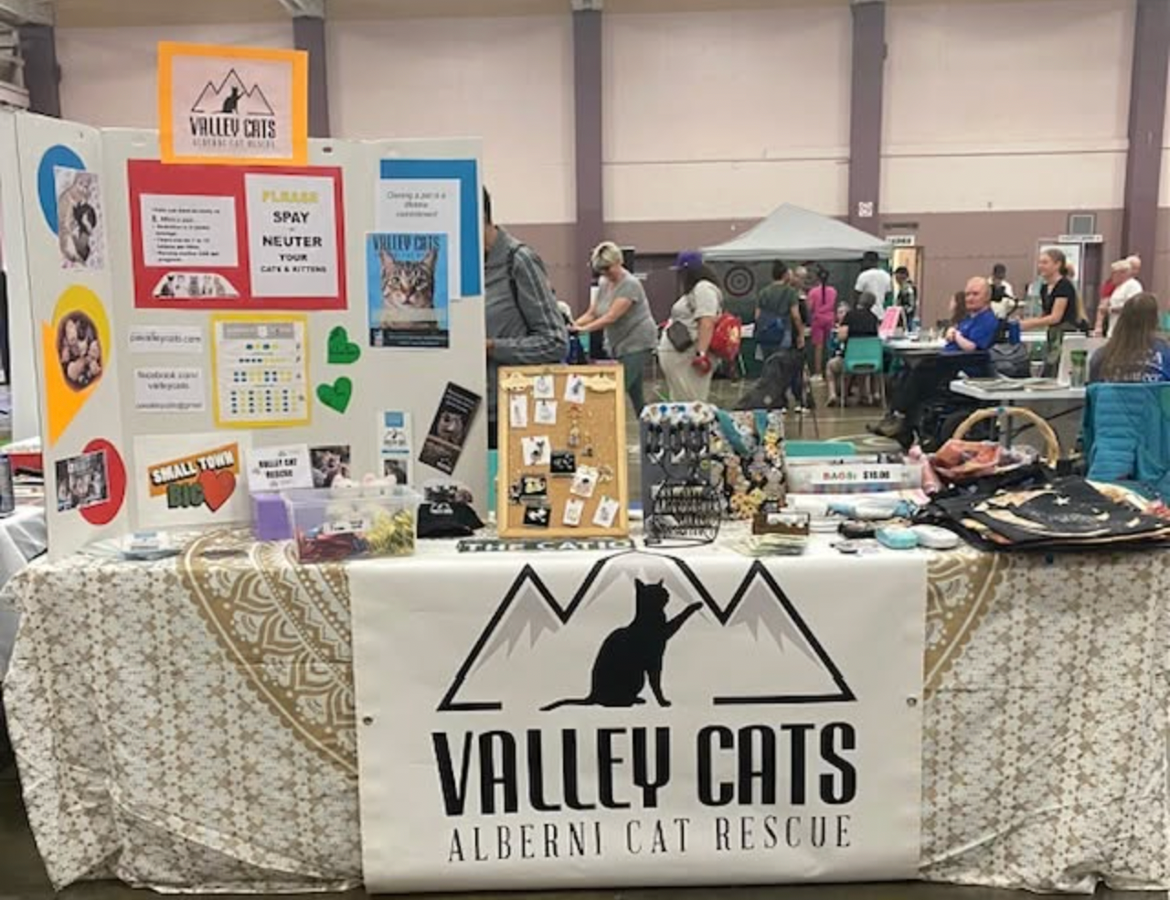 Valley Cats Alberni Cat Rescue booth at an indoor event, featuring adoption info, merchandise, and cat-themed displays.