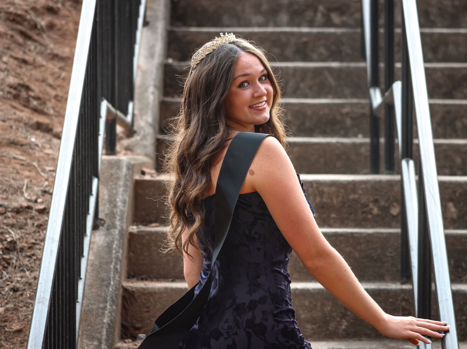Homecoming queen portrait on stairs looking back at the camera with elegance,  captured by L&C Moments Photography in McDonough, GA.
