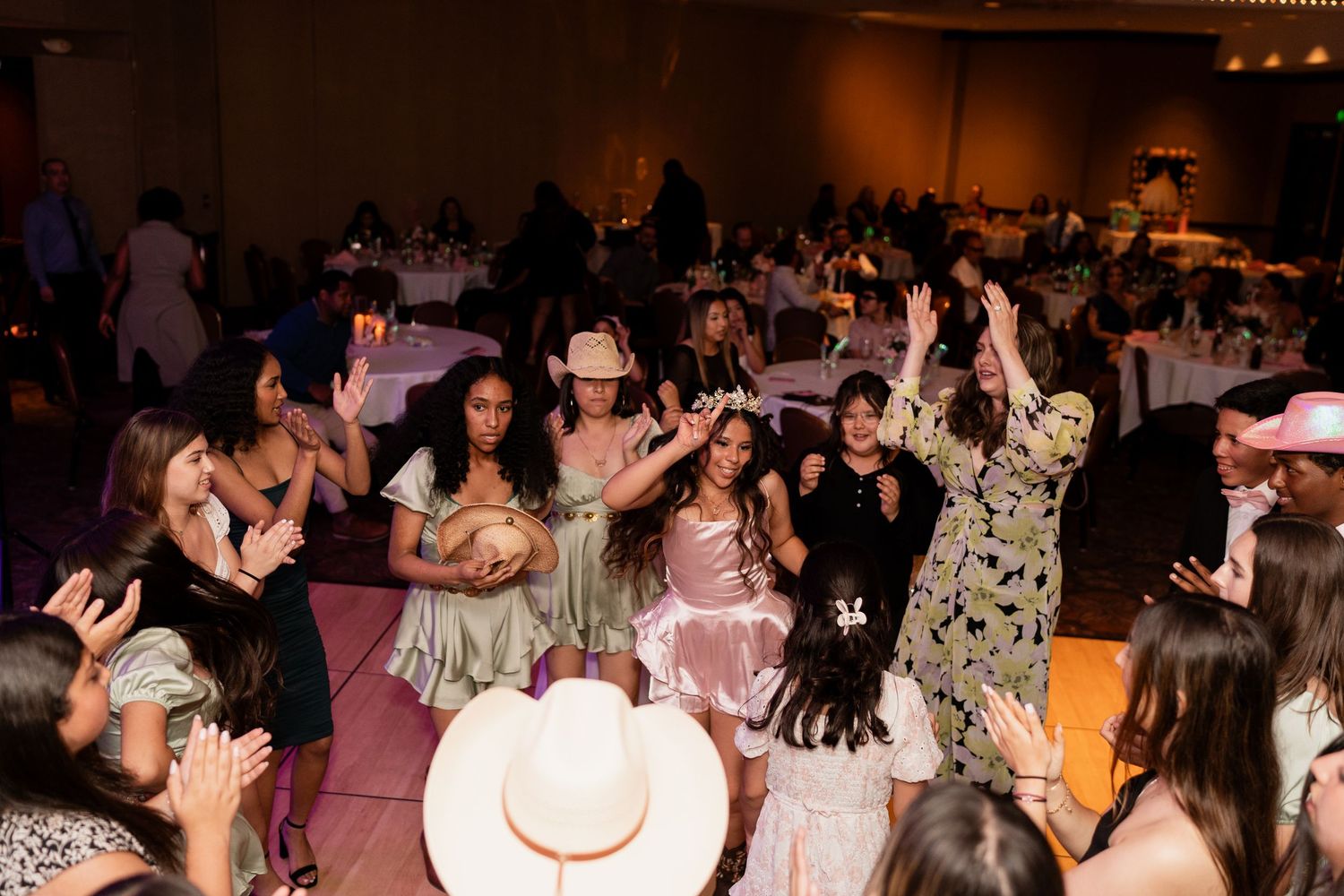 Wedding guests dance and celebrate together on a pink-lit dance floor at an indoor reception venue.