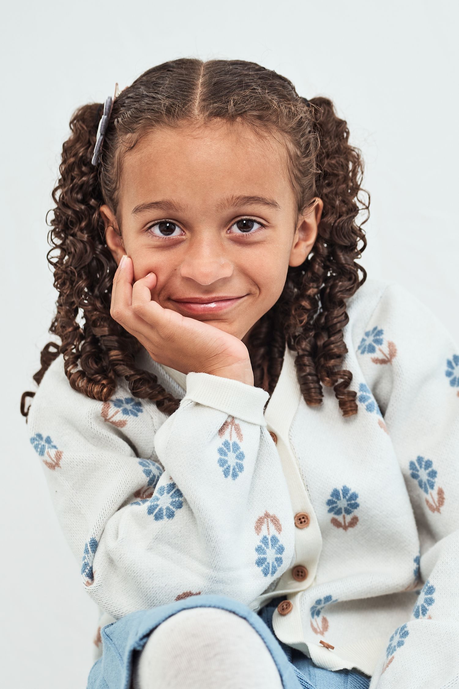Child wearing a white floral sweater makes playful expressions in a series of connected portrait photos.