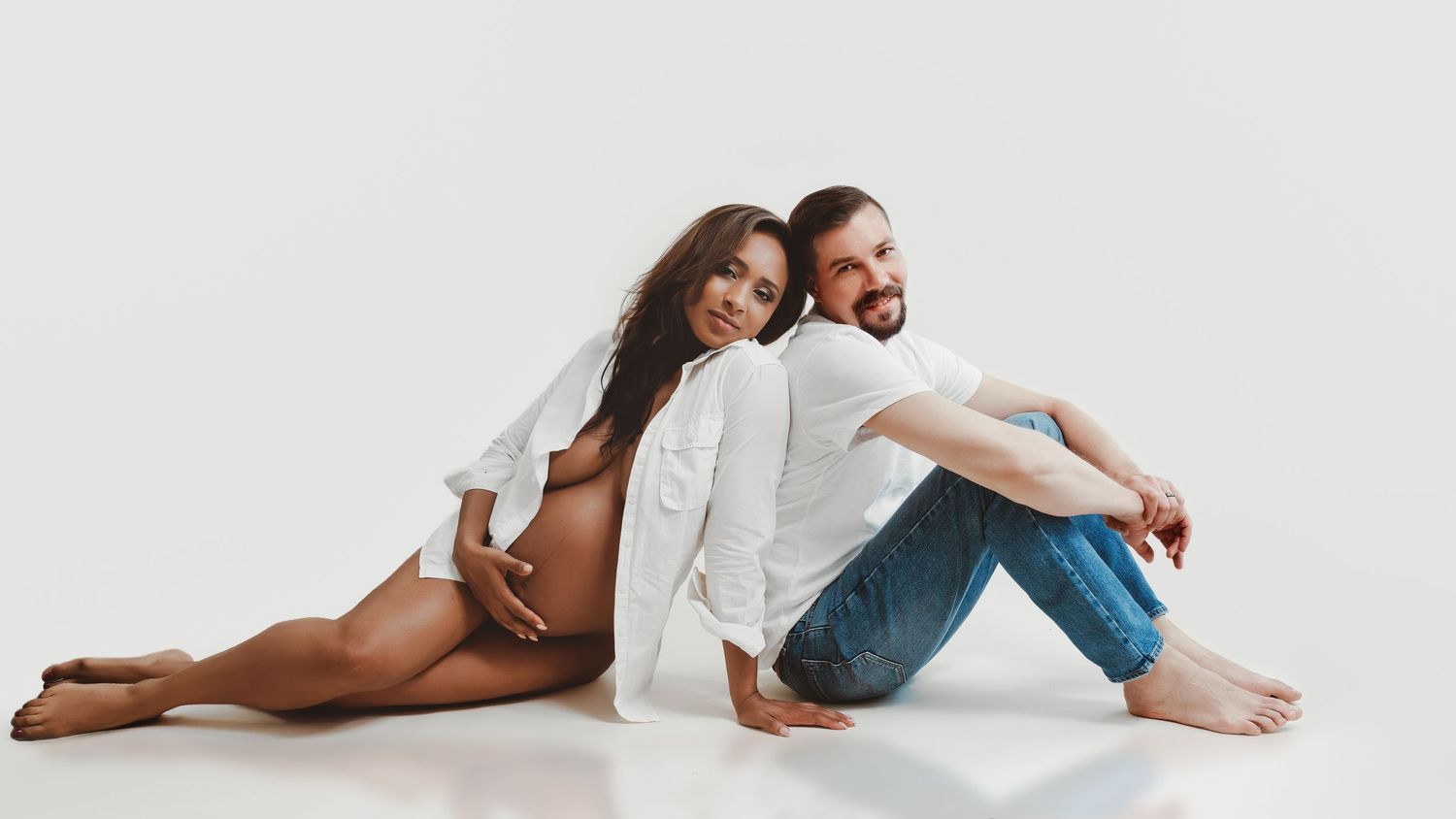 Intimate couples photoshoot with partners sitting back to back in casual white attire.