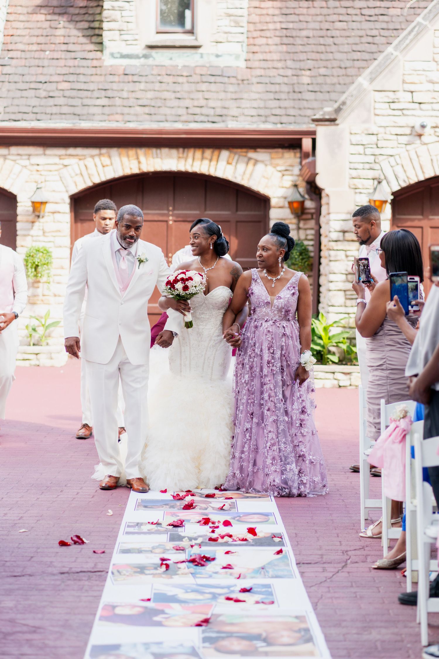 A wedding ceremony procession walks down an aisle decorated with rose petals and photos.