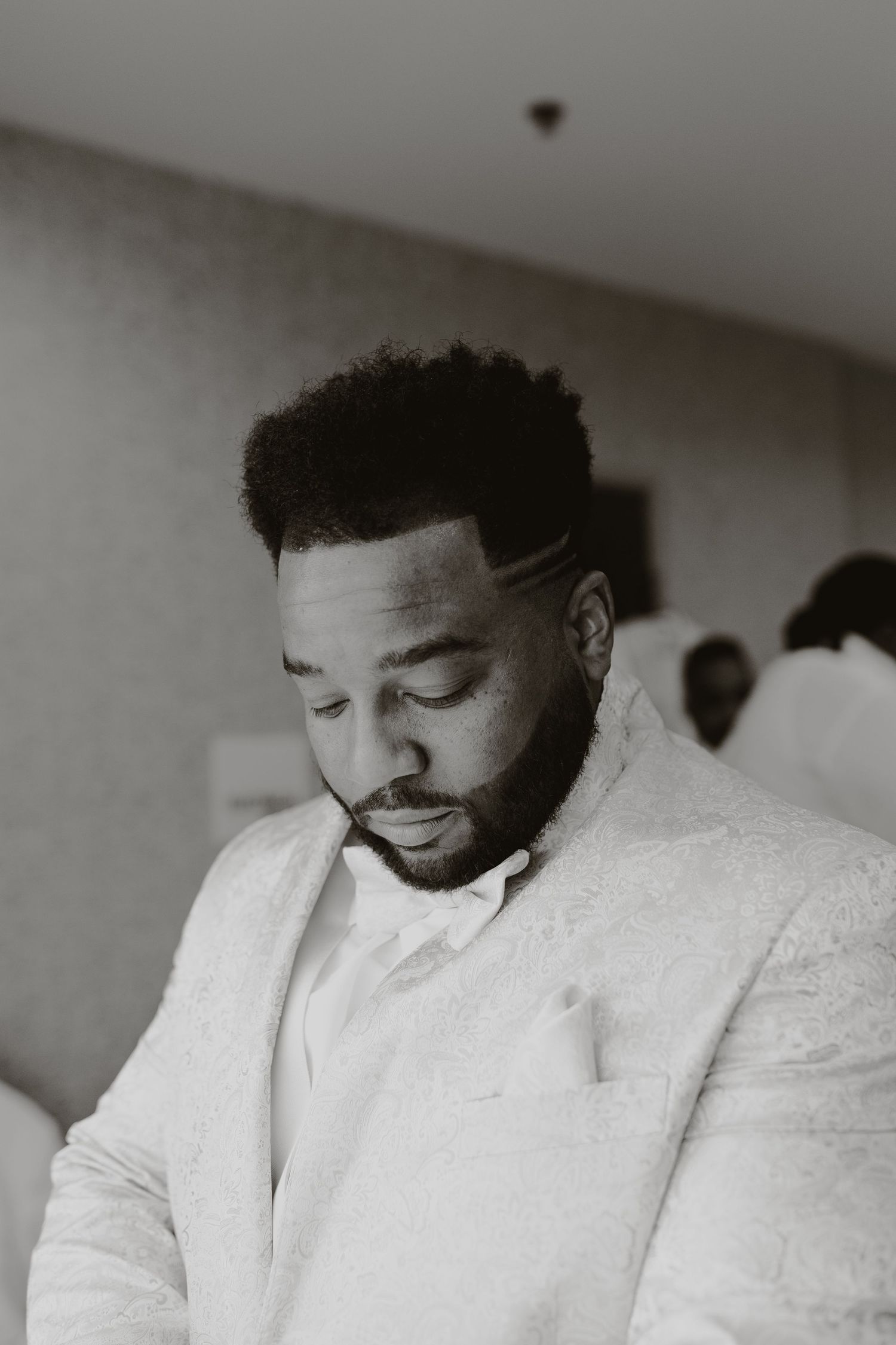 Person in a white formal jacket and bowtie looking down in a contemplative moment.
