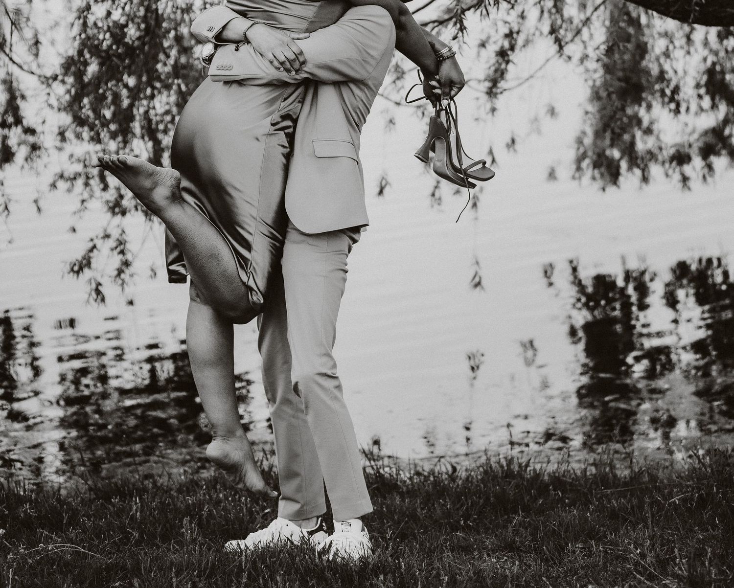 Black and white romantic portrait of couple's legs embracing outdoors near water.
