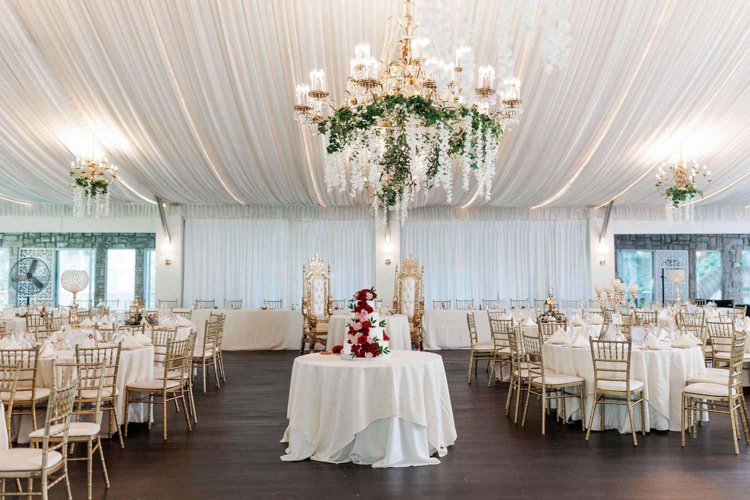 Romantic wedding reception setup with white draping, chandeliers and a red-accented cake display.