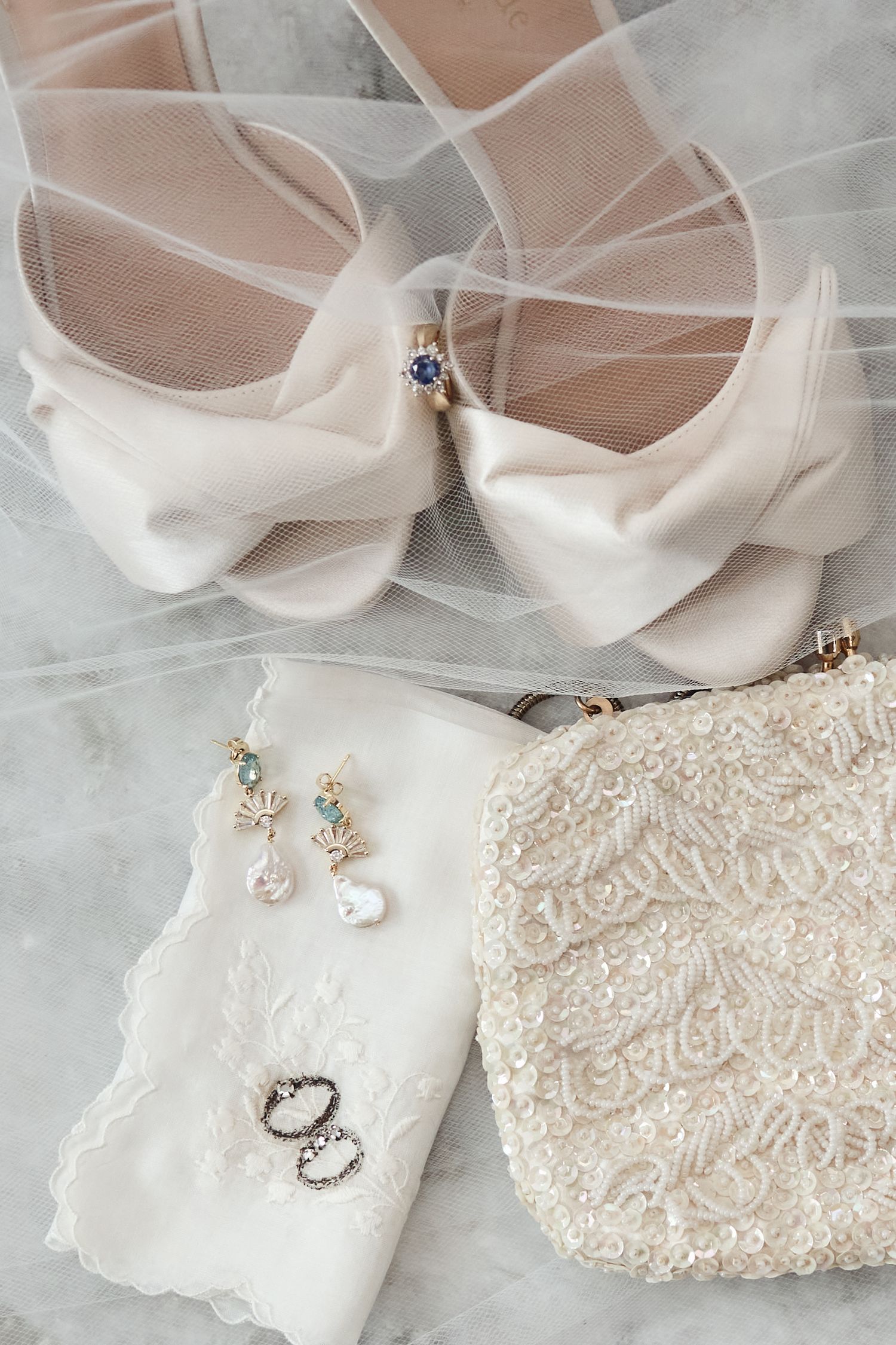 Elegant wedding accessories including white lace details, delicate jewelry, and satin shoes arranged on light fabric.