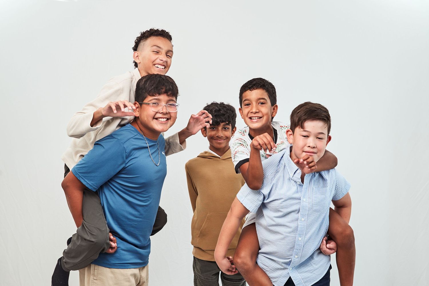 Five friends posing playfully together wearing casual clothing against a light colored backdrop.