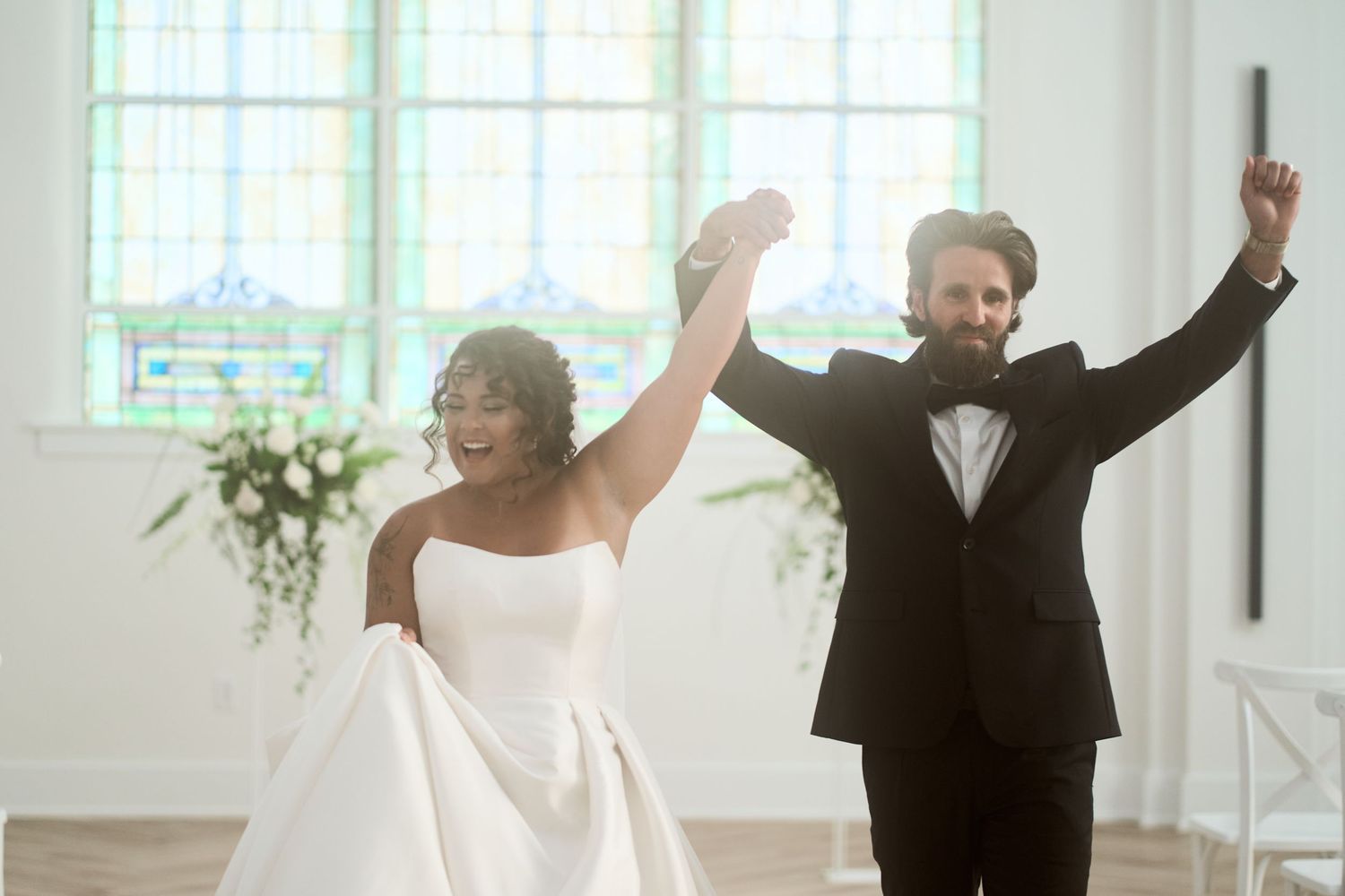 Celebratory moment in a bright chapel as newlyweds raise their arms in triumph.