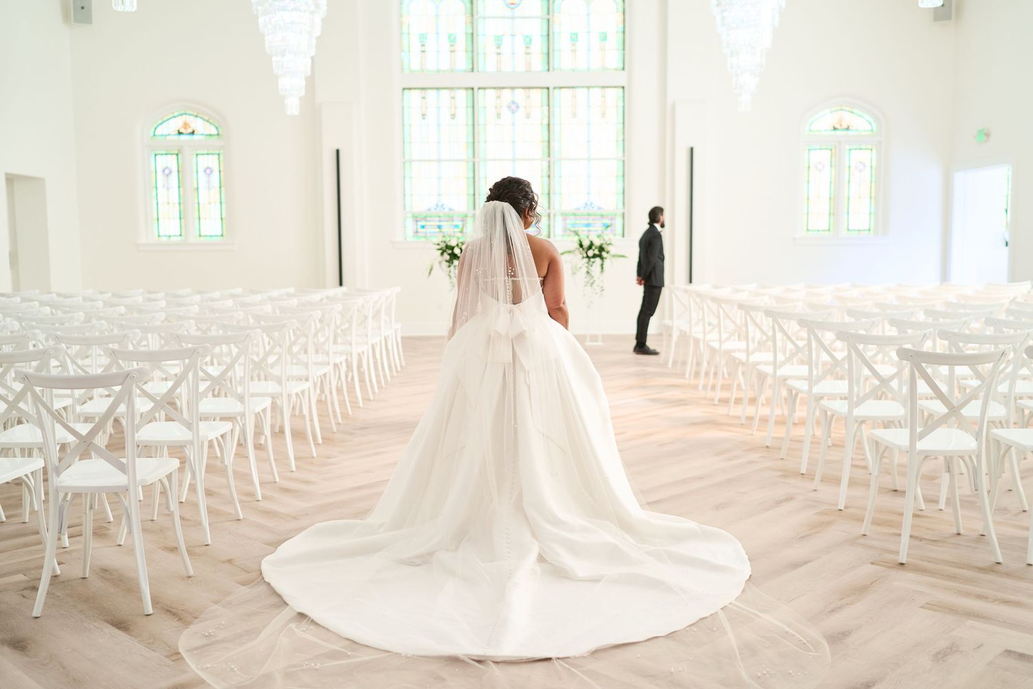 Romantic wedding ceremony moment with couple embracing in front of stained glass windows and floral arrangements.