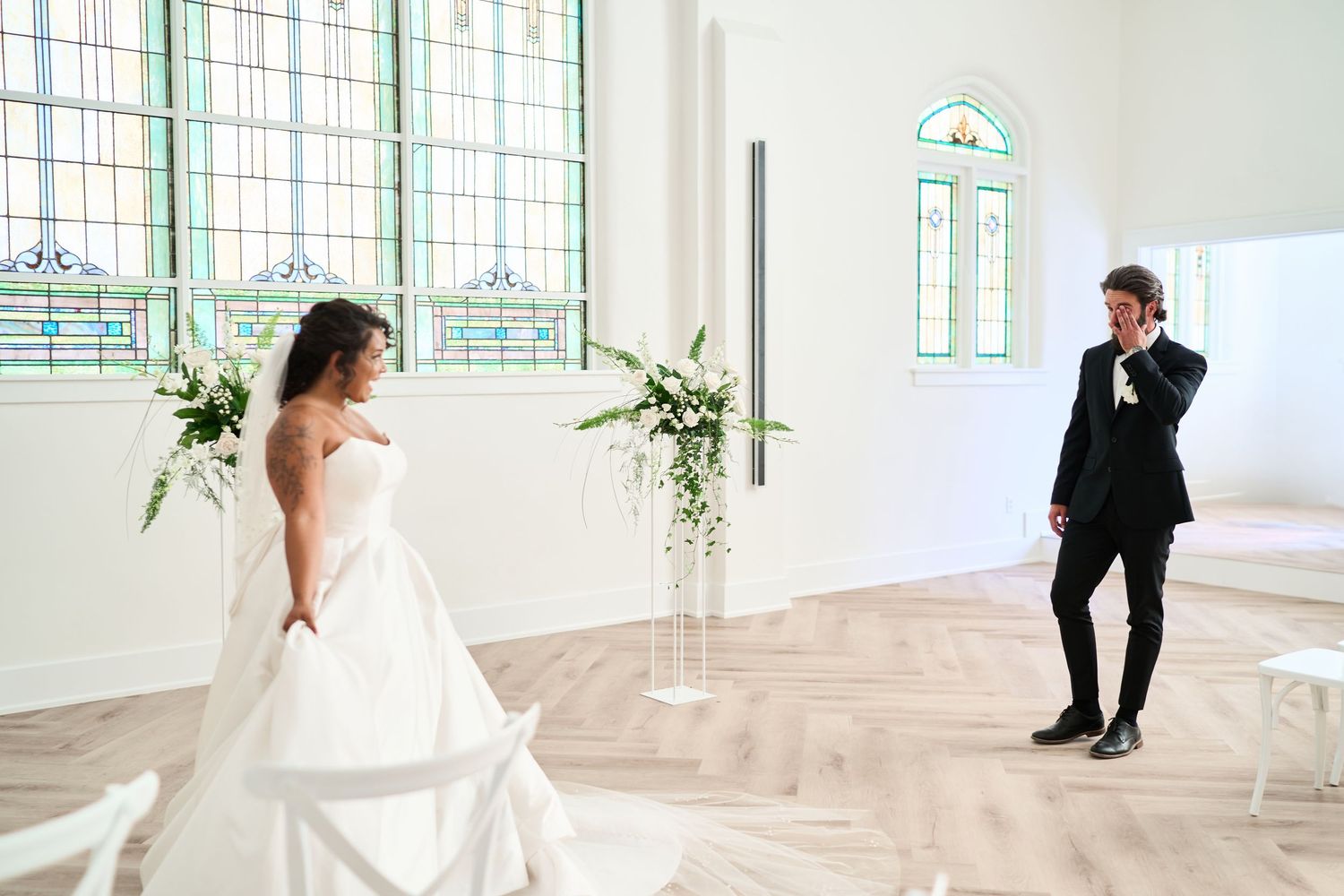 A wedding first look moment in a bright chapel with stained glass windows and herringbone floors.