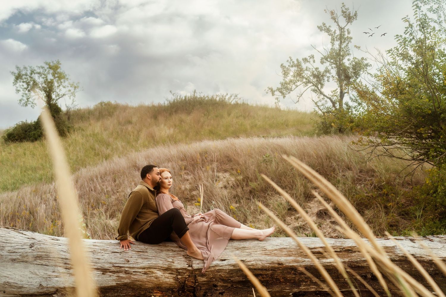 Couple sitting together on fallen log in rustic outdoor setting with tall grass.