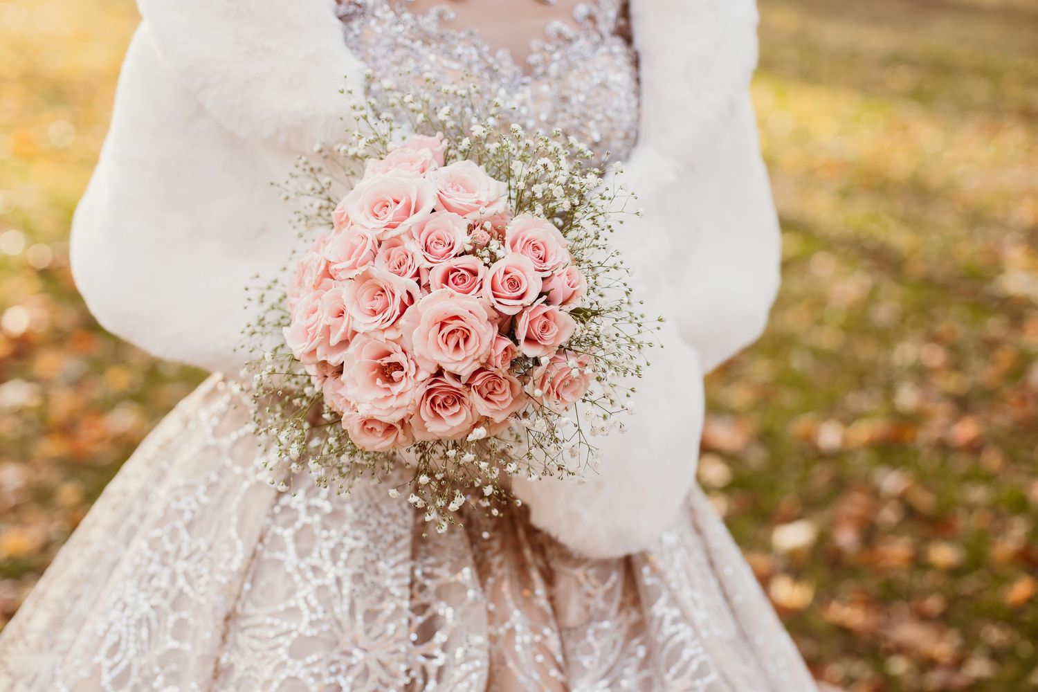 Close-up of pink rose and baby's breath wedding bouquet with lace dress detail.