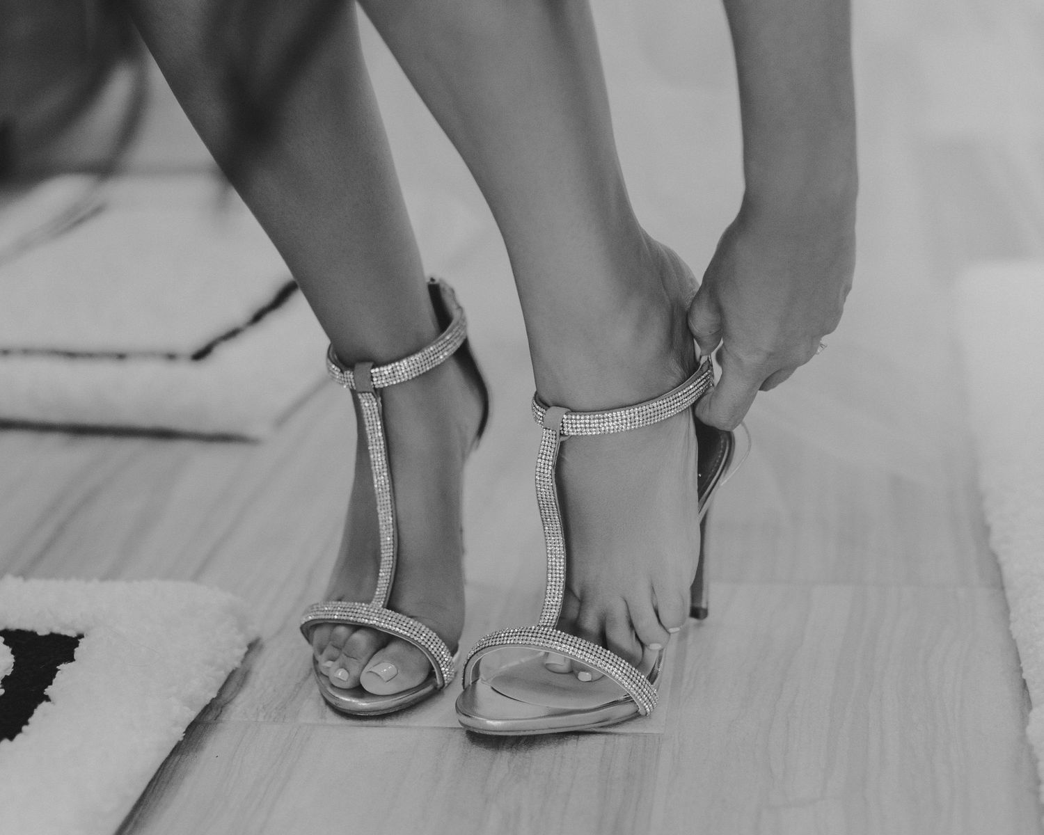 Close-up of sparkly bridal shoes being fastened on hardwood floor.