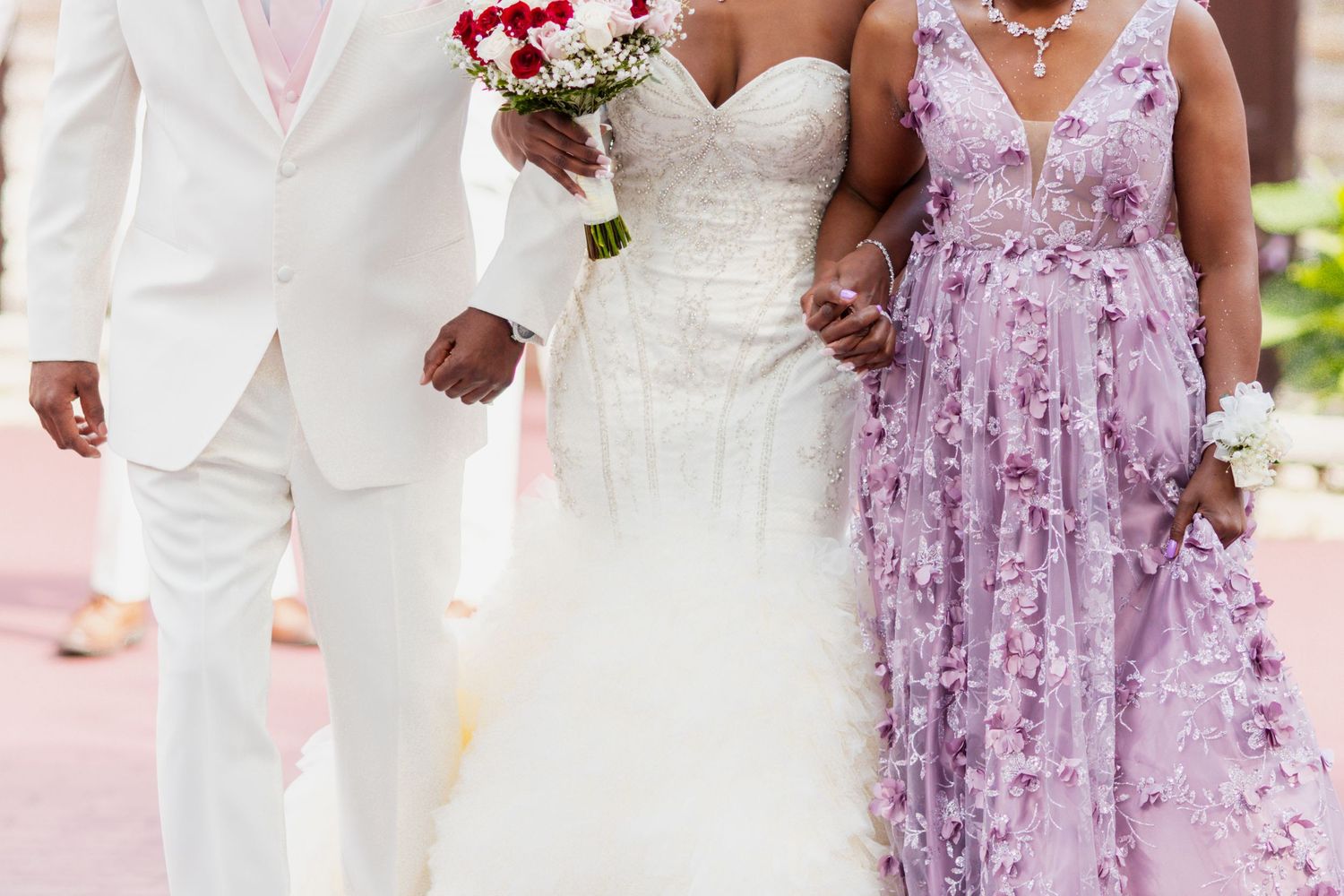 Close-up of elegant wedding attire including a white suit, bridal gown, and purple floral dress.