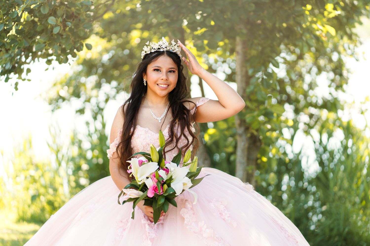 Wedding party poses outdoors under green trees in natural lighting.