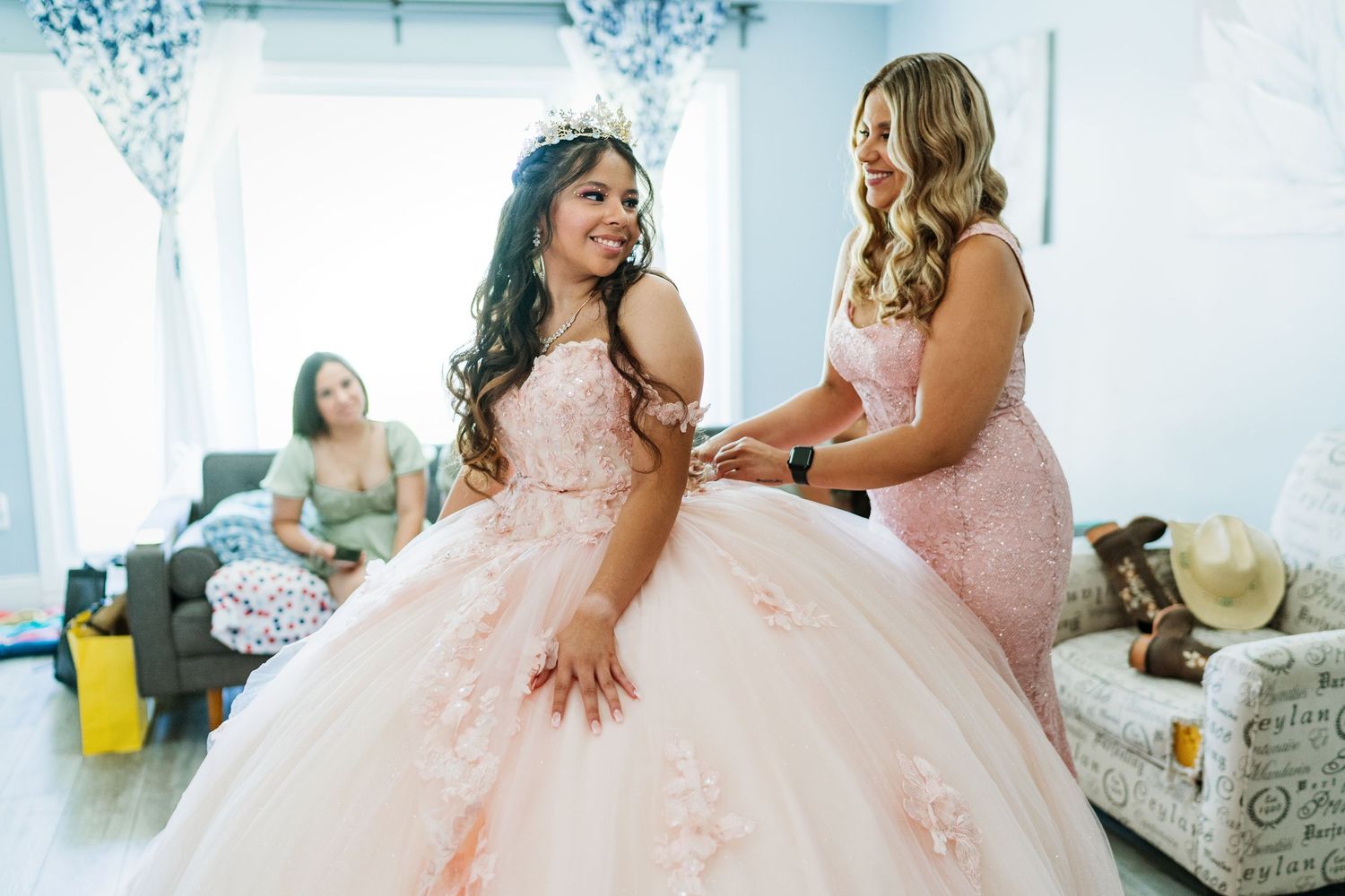 Young woman in a flowing pink ballgown getting ready in a bright white room.