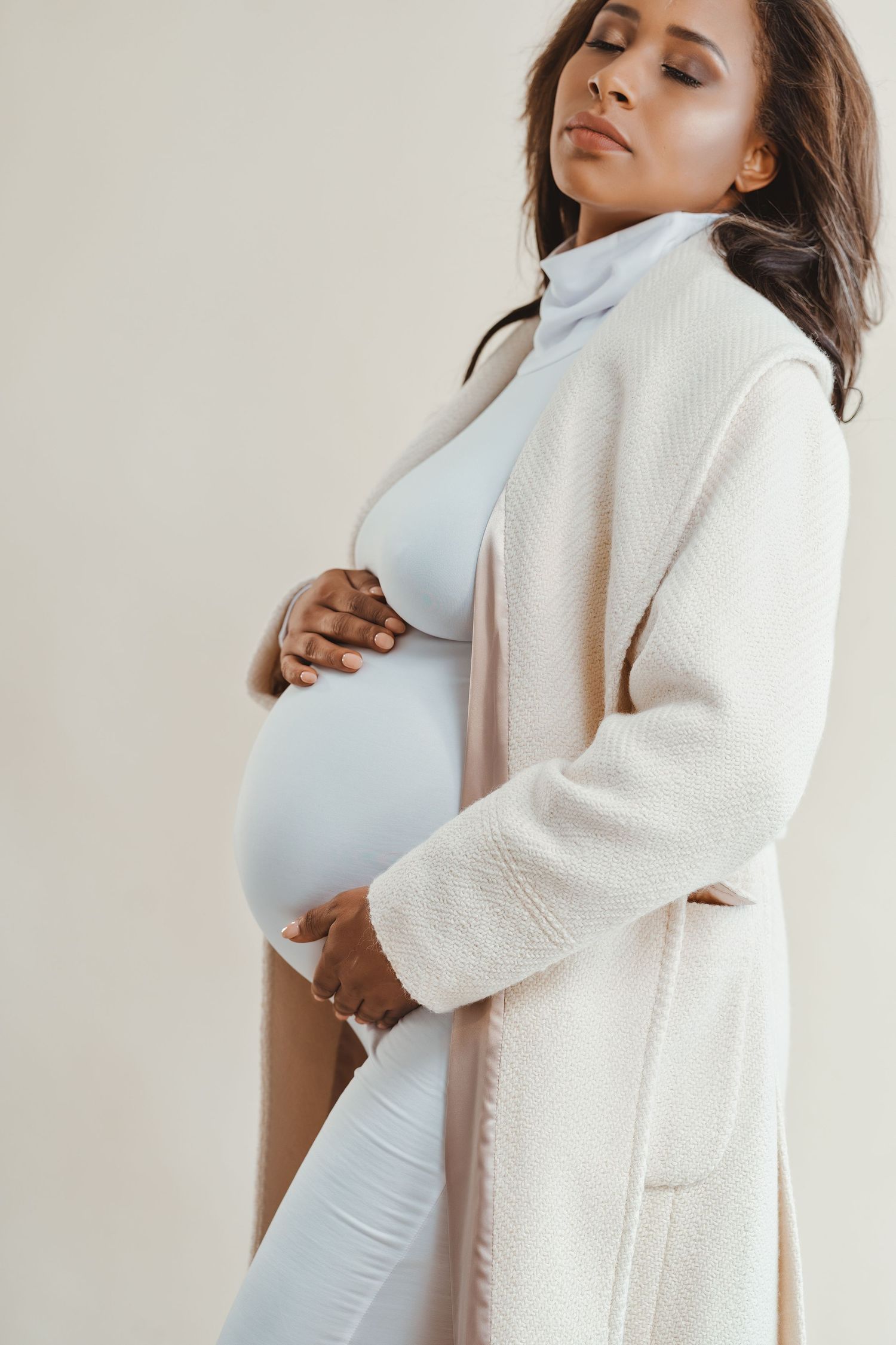 Elegant maternity portrait of woman in white coat cradling baby bump.