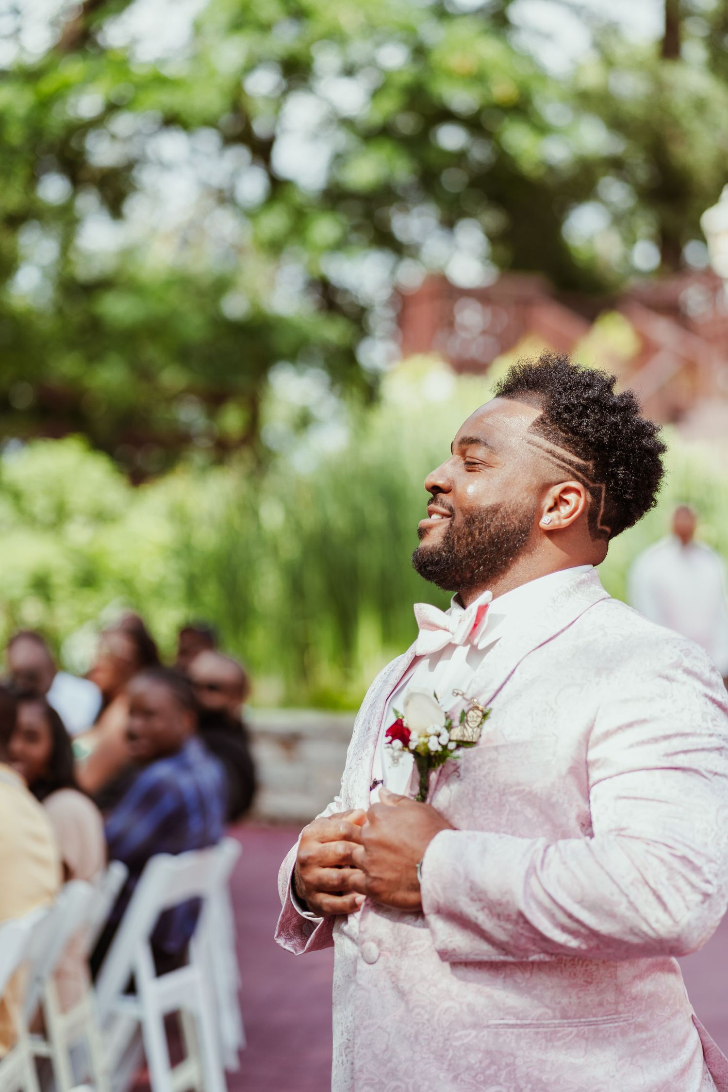 A joyful groom in a light pink suit jacket laughs during an outdoor wedding ceremony.