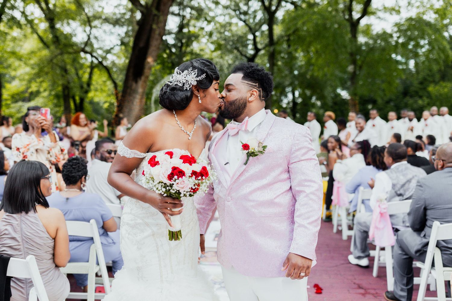 Wedding couple shares an intimate moment on the aisle surrounded by guests at an outdoor ceremony.