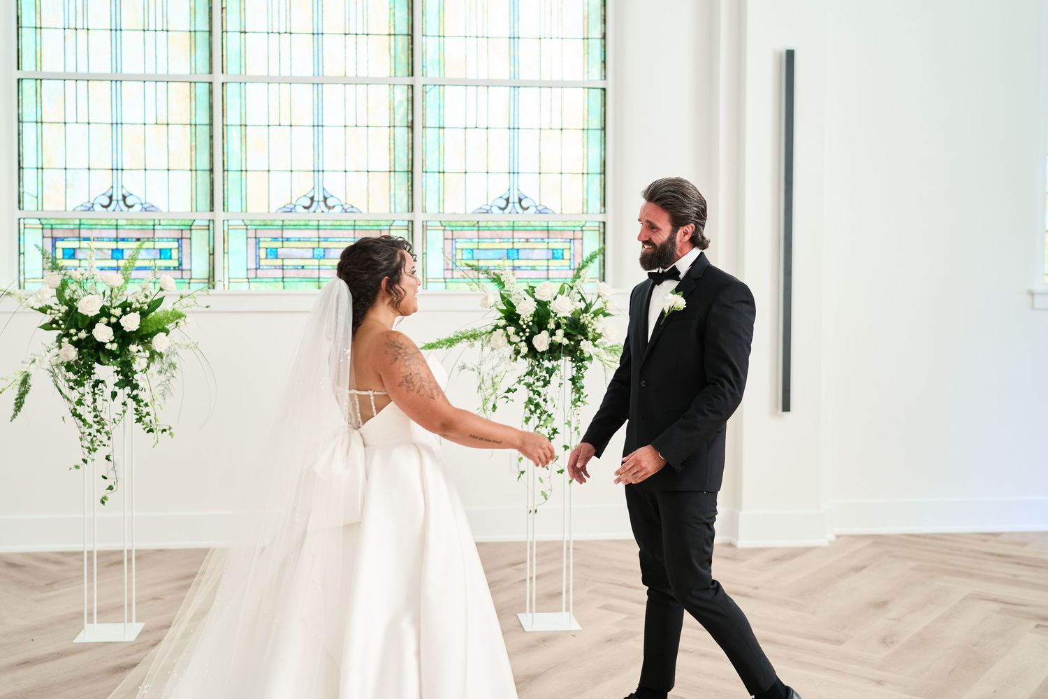 A couple shares their first moments together in a chapel with stained glass windows and white floral arrangements.