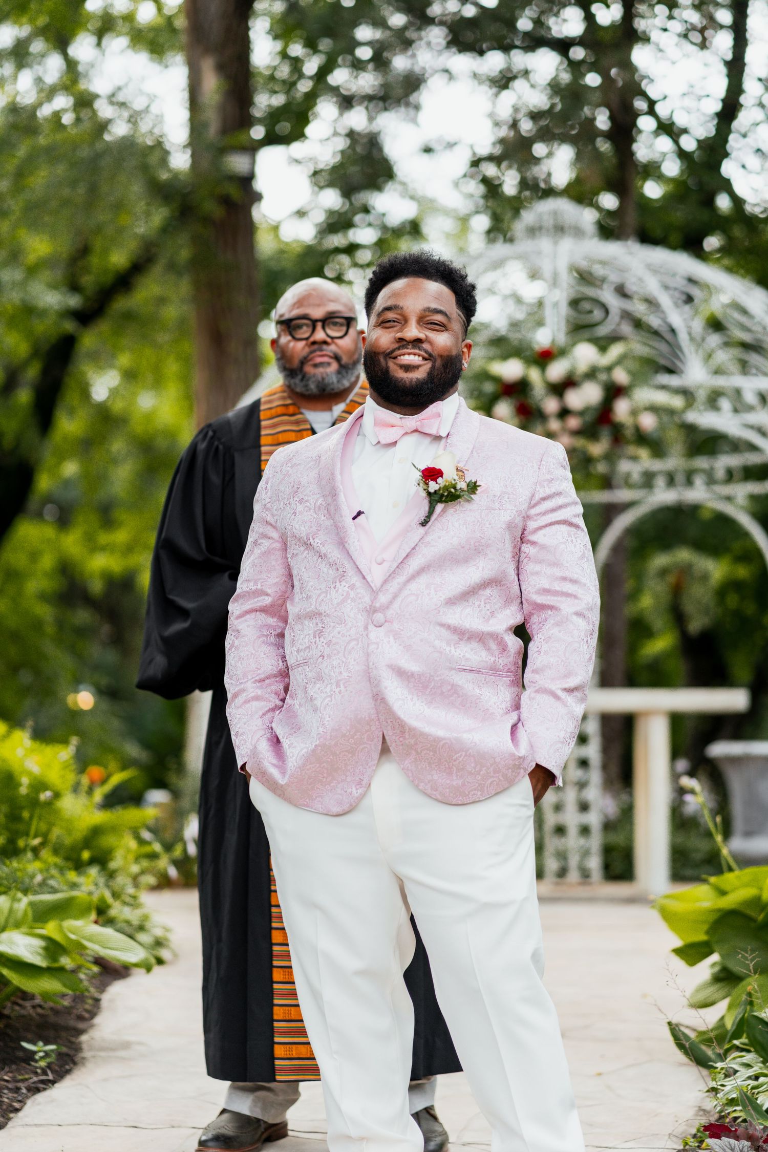Wedding ceremony portrait in garden setting with decorative white arbor.