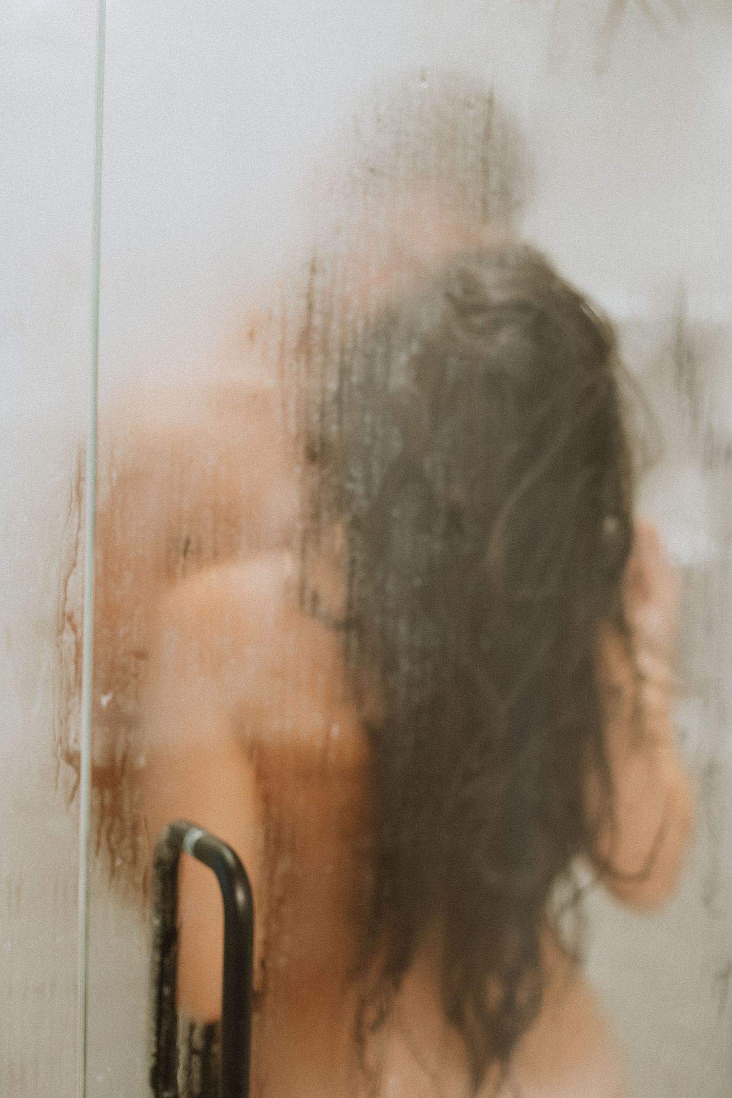Silhouette of a person behind foggy shower glass.
