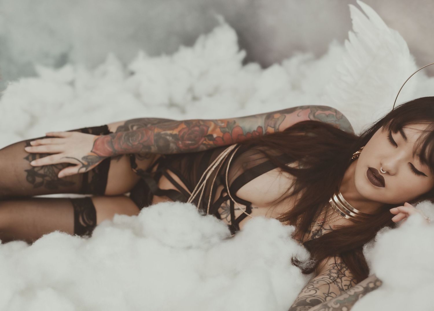 A moody boudoir photo of a tattooed model posing dramatically in white clouds.