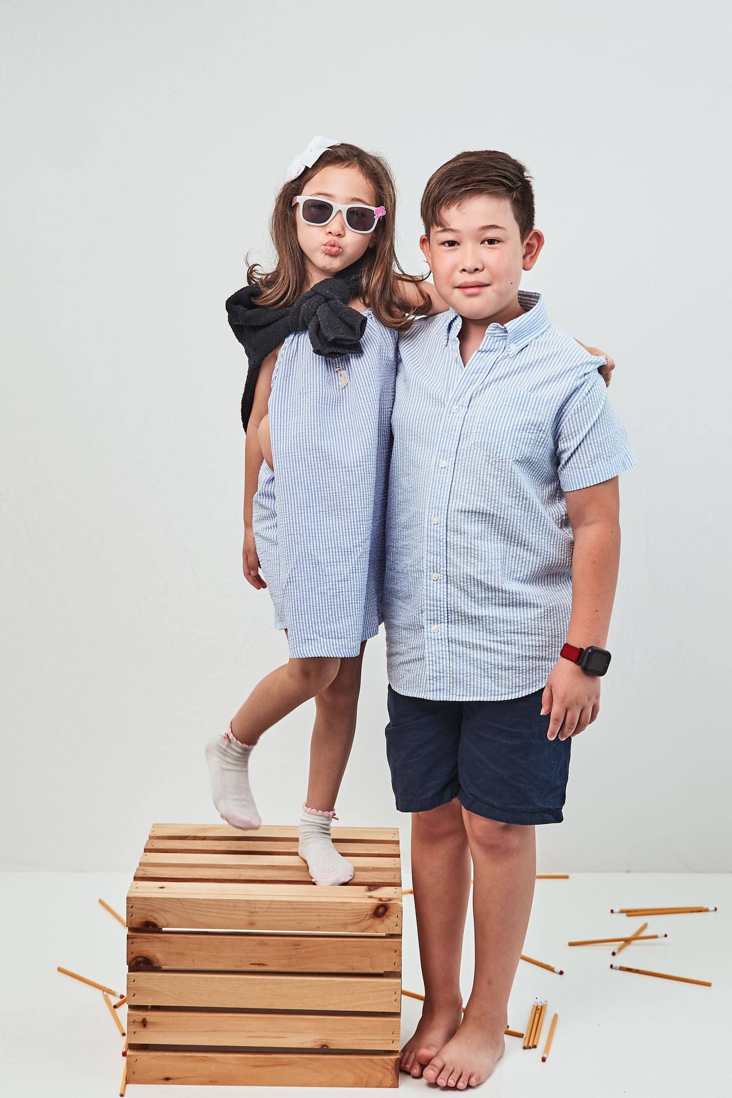 A parent and child in coordinating blue outfits stand together holding wooden crates with casual elegance.