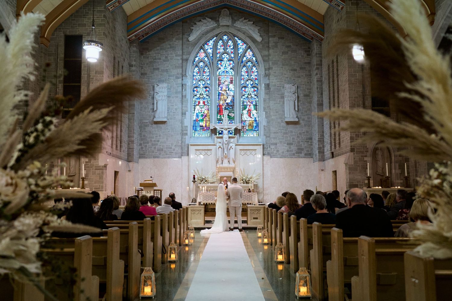 Elegant church interior with stone columns and stained glass windows illuminated for a wedding ceremony.