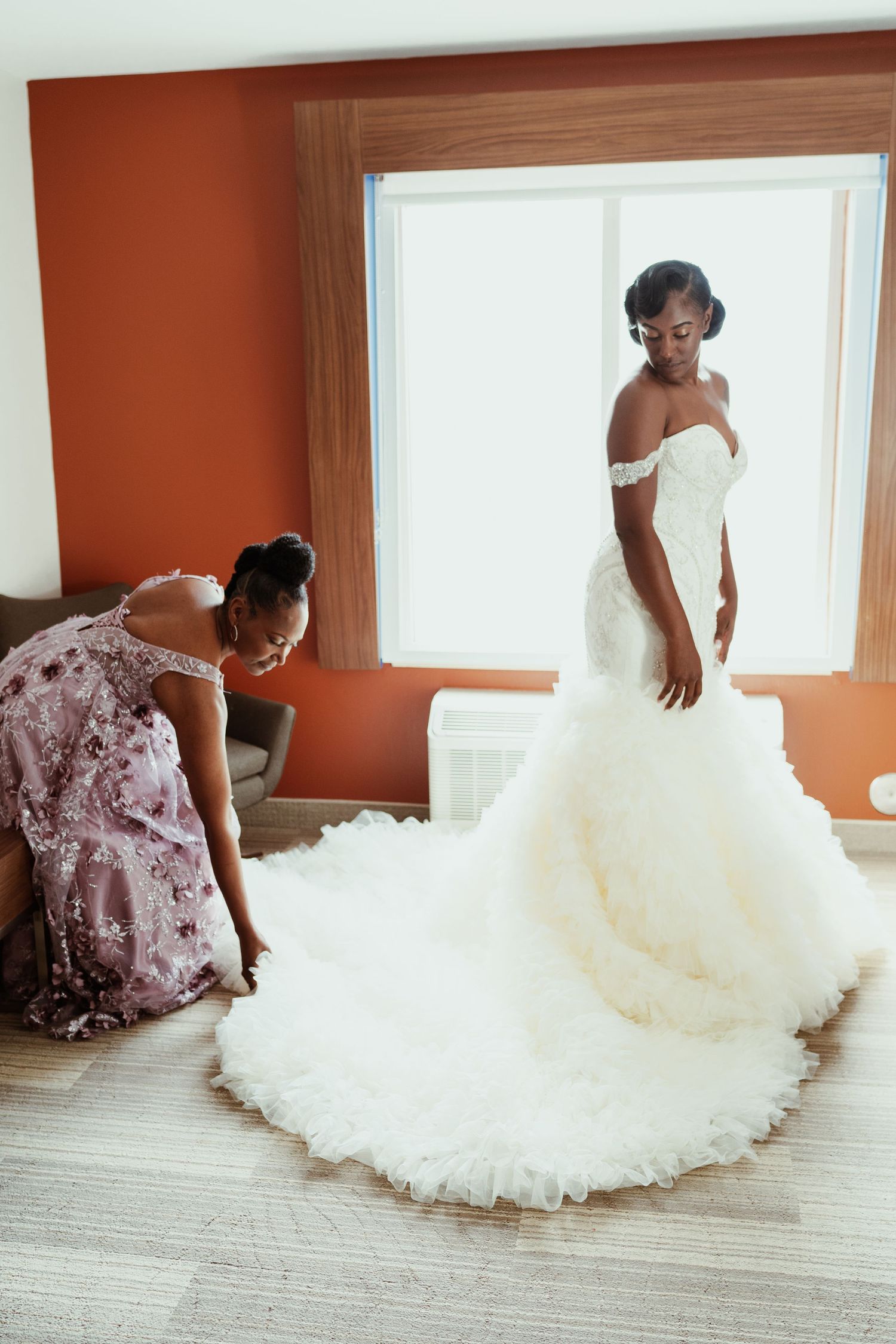 A stunning mermaid wedding dress with off-shoulder detail and flowing train in a sunlit room.