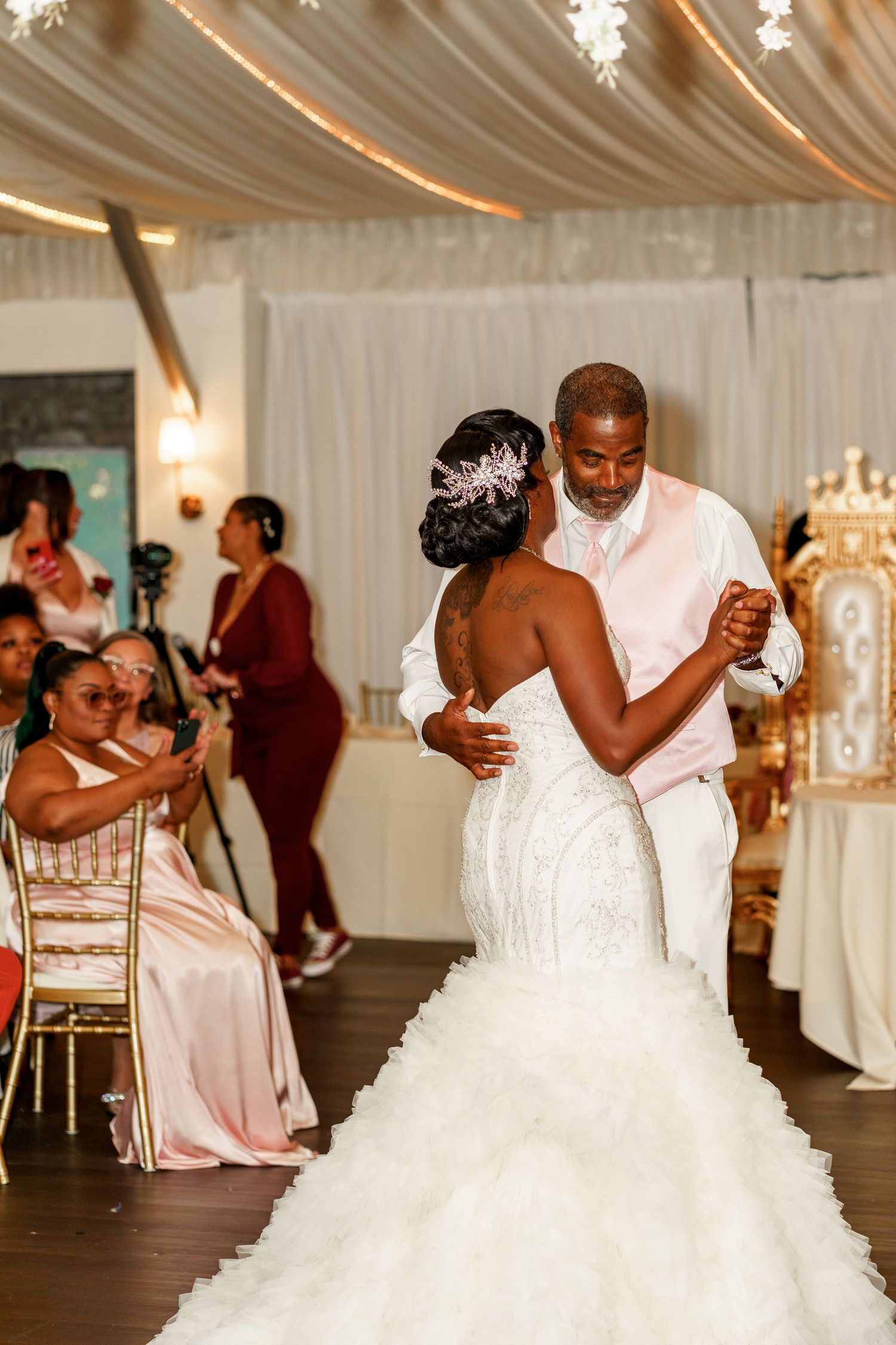 Elegant wedding reception dance with guests watching as couple dances under draped fabric ceiling and chandeliers.