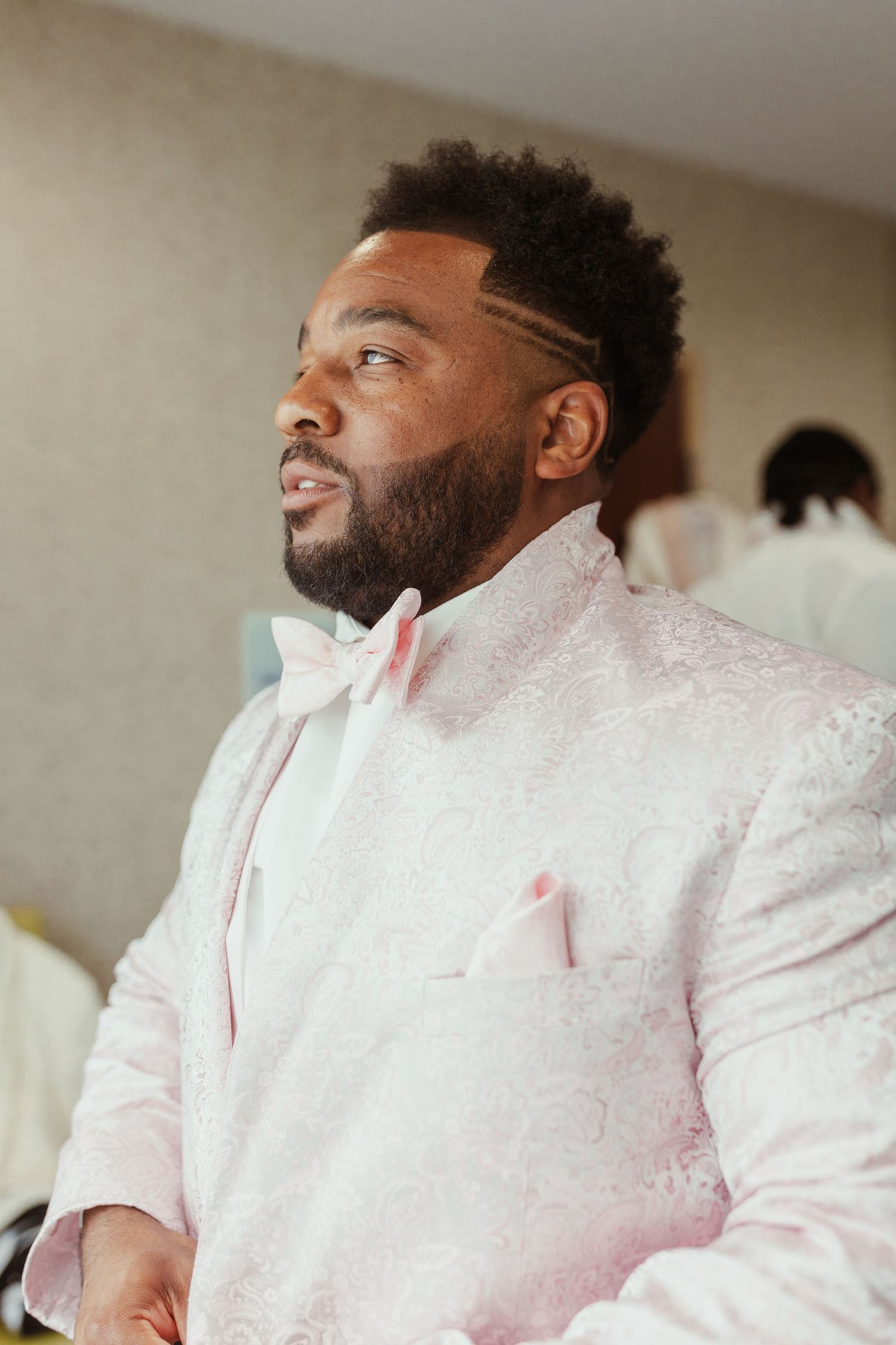 Person wearing an elegant white textured suit jacket with pink accents looking to the side.
