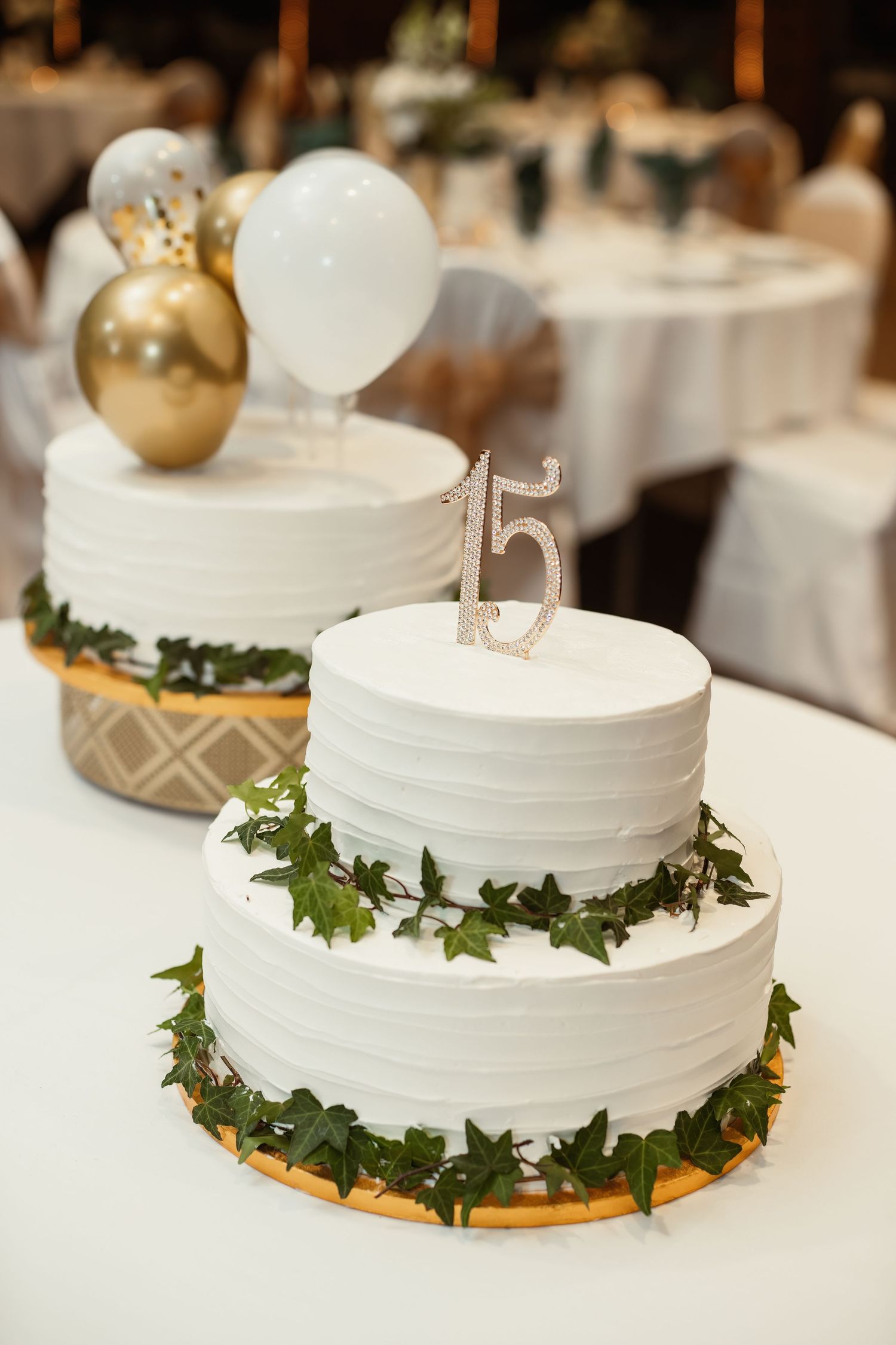 Elegant white tiered wedding cake decorated with greenery and gold accents.