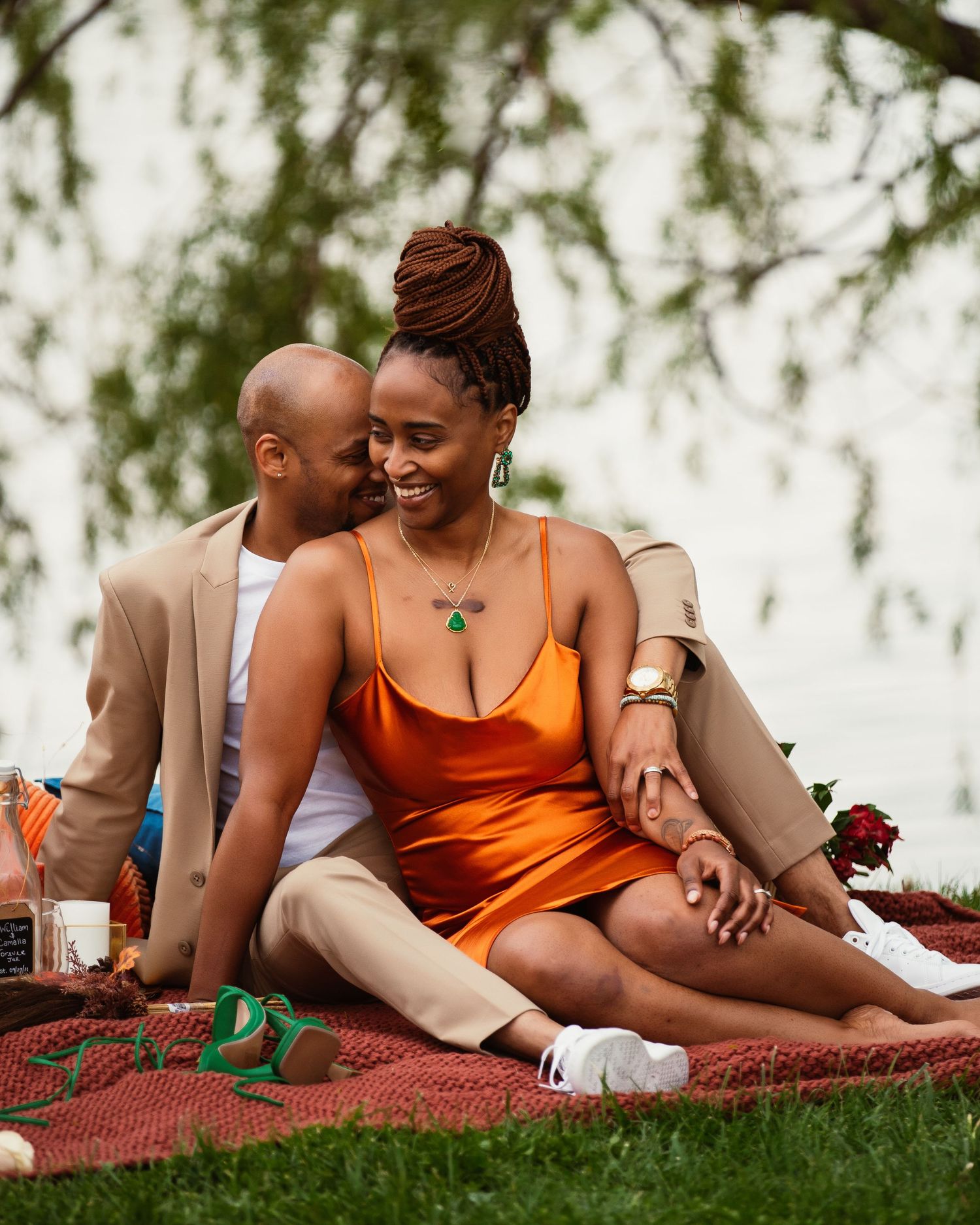 Couple sharing intimate moment on picnic blanket in orange and tan outfits.