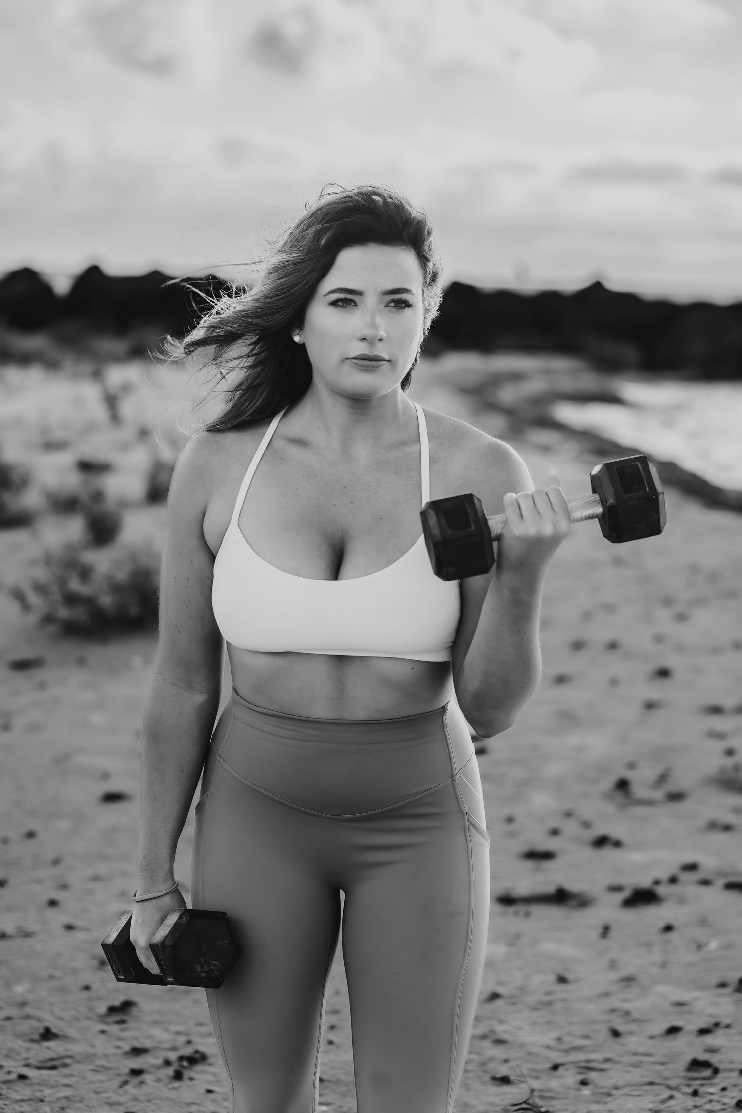 Woman exercising with dumbbells on beach in black and white photography.