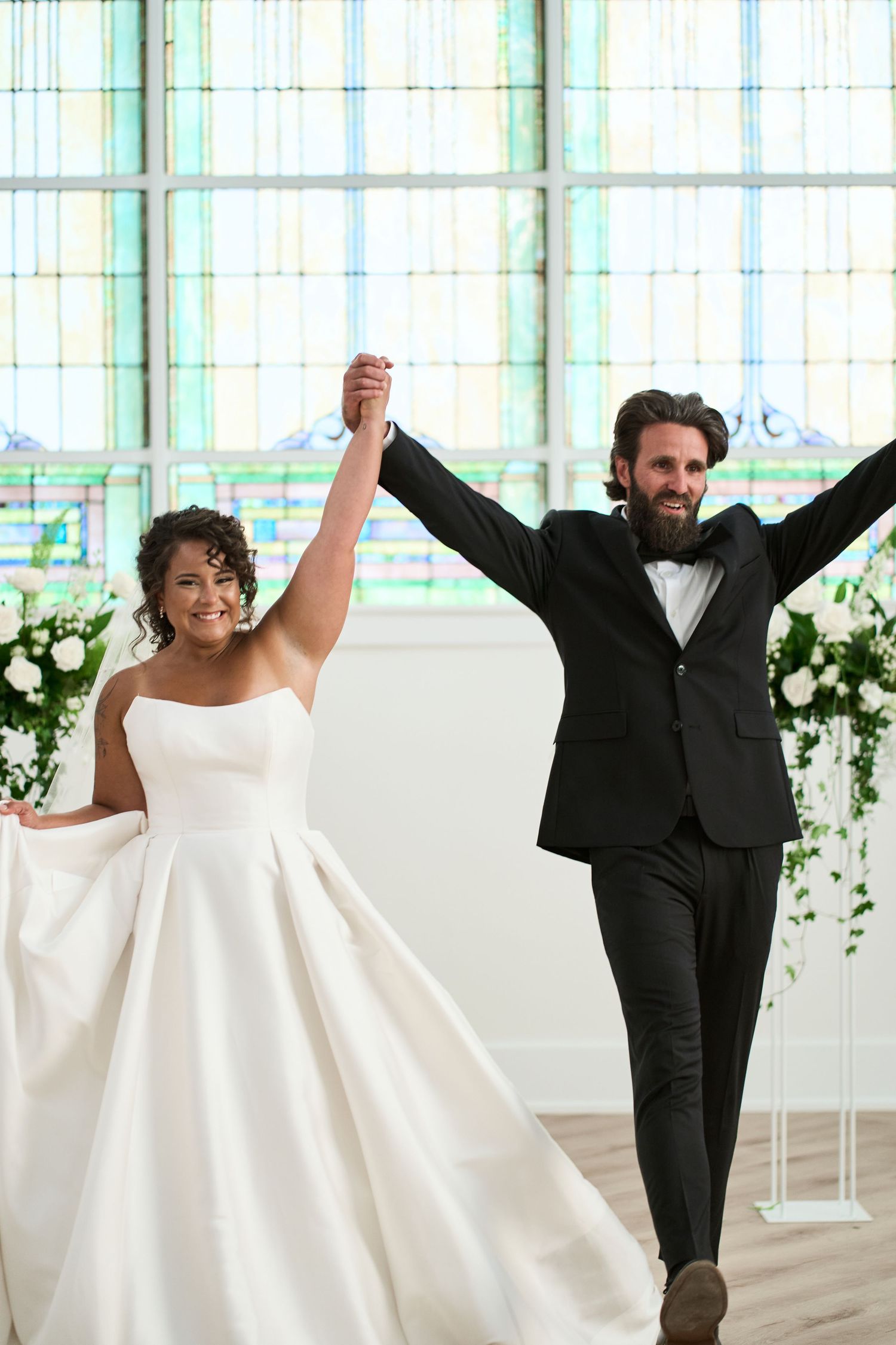 Joyful newlyweds celebrate with raised arms during their wedding ceremony in a light-filled venue.