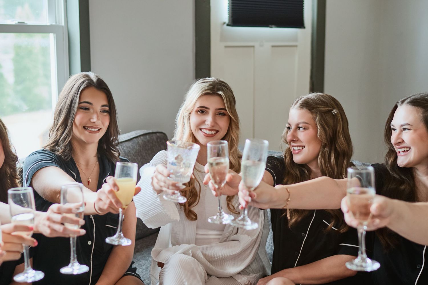 Group of friends raising champagne glasses in a celebratory toast by a bright window.