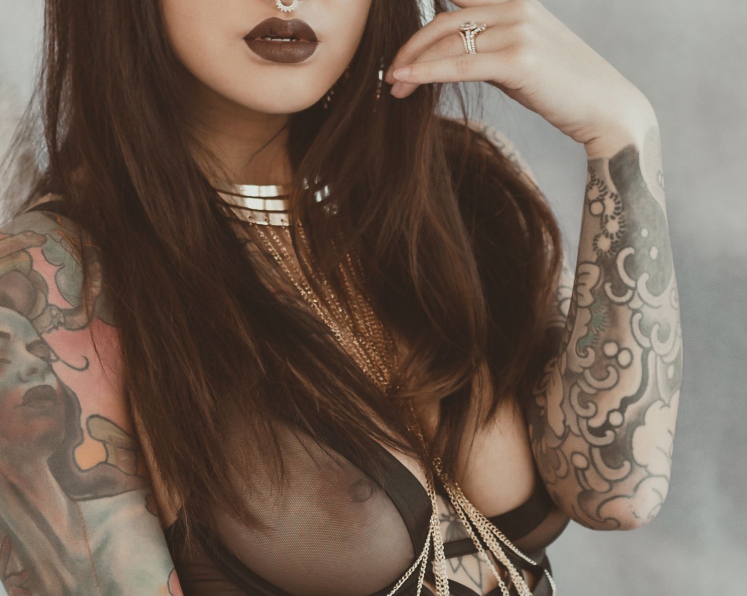 Close up portrait showing gothic makeup and intricate tattoo sleeve details in moody lighting.
