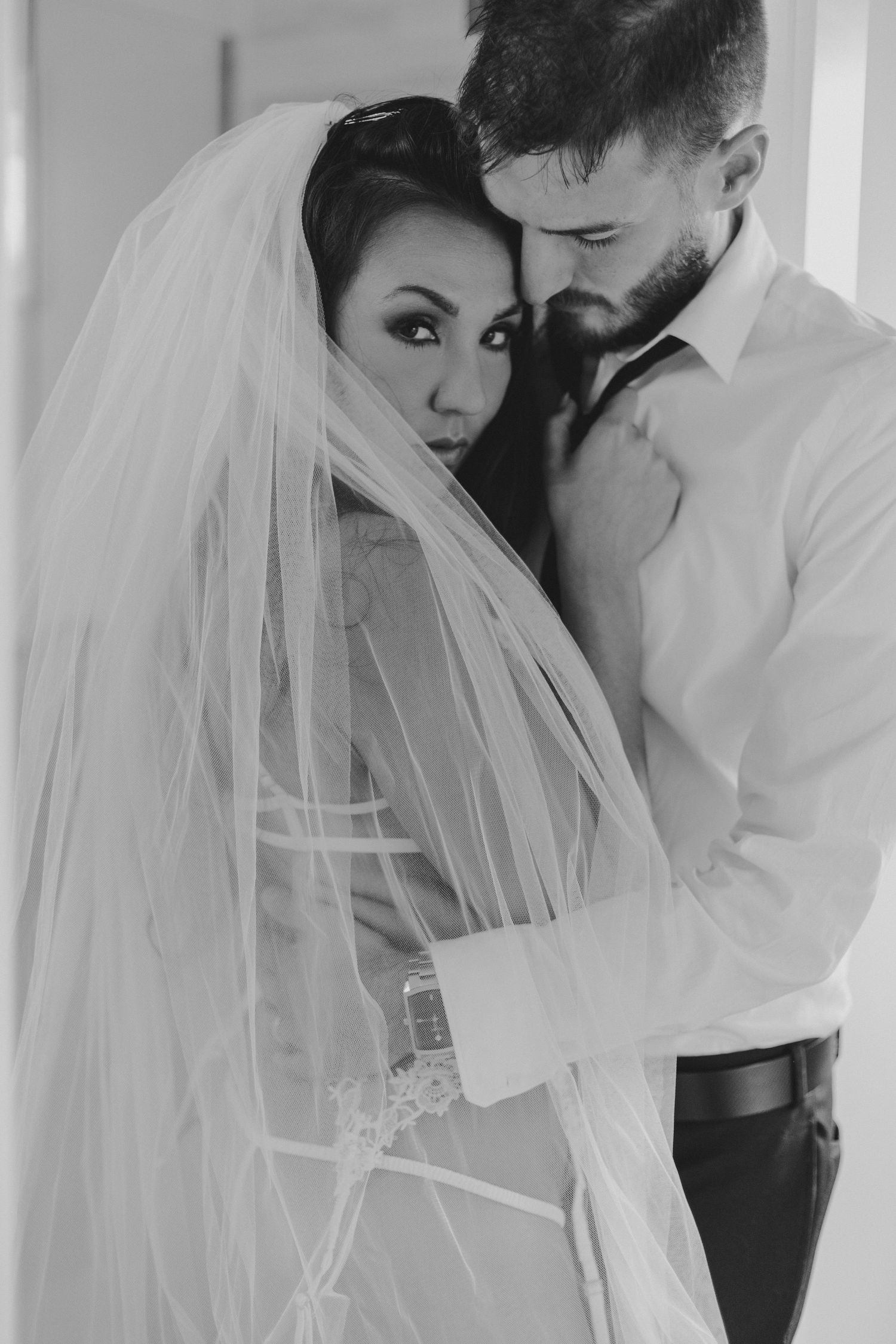 Black and white wedding portrait of couple in intimate pose with flowing veil.