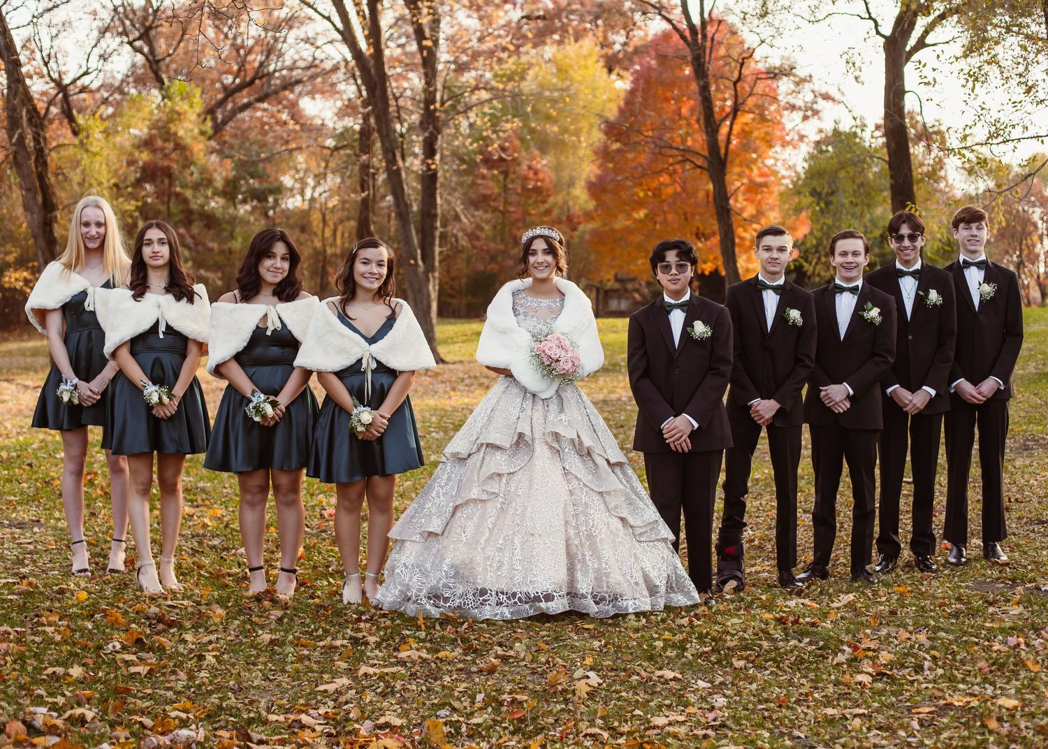 Wedding party in black and navy attire posed among autumn trees.