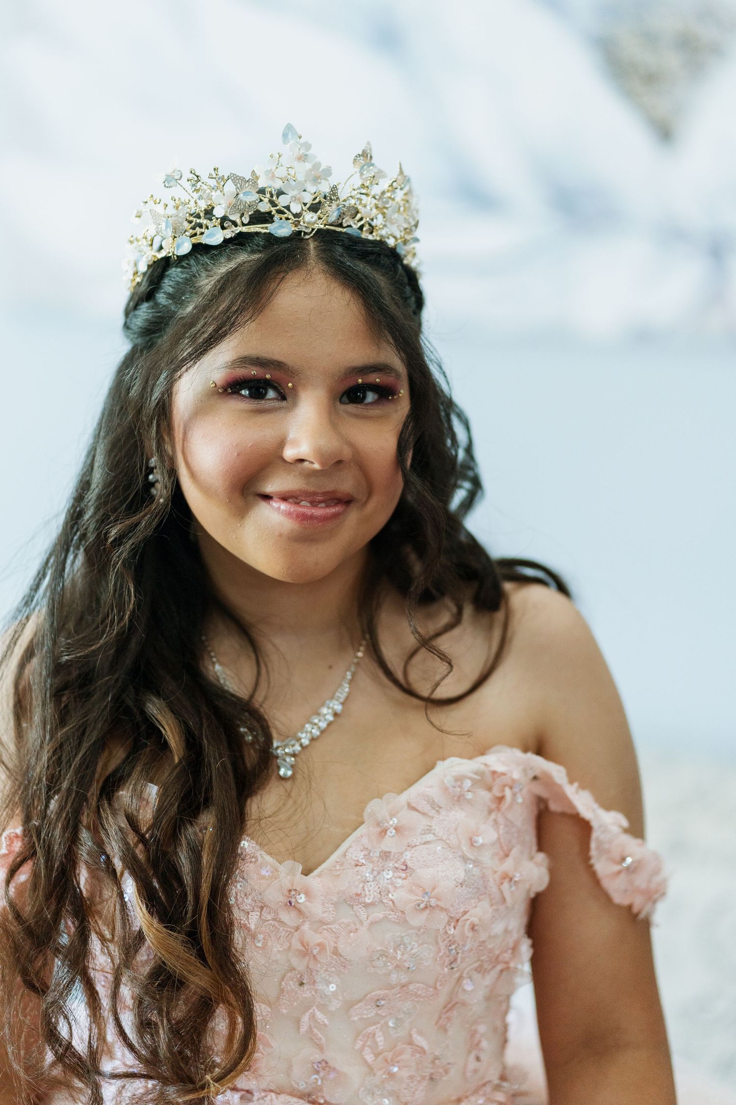A stunning quinceañera portrait showcasing an ornate crown and delicate pink off-shoulder gown.