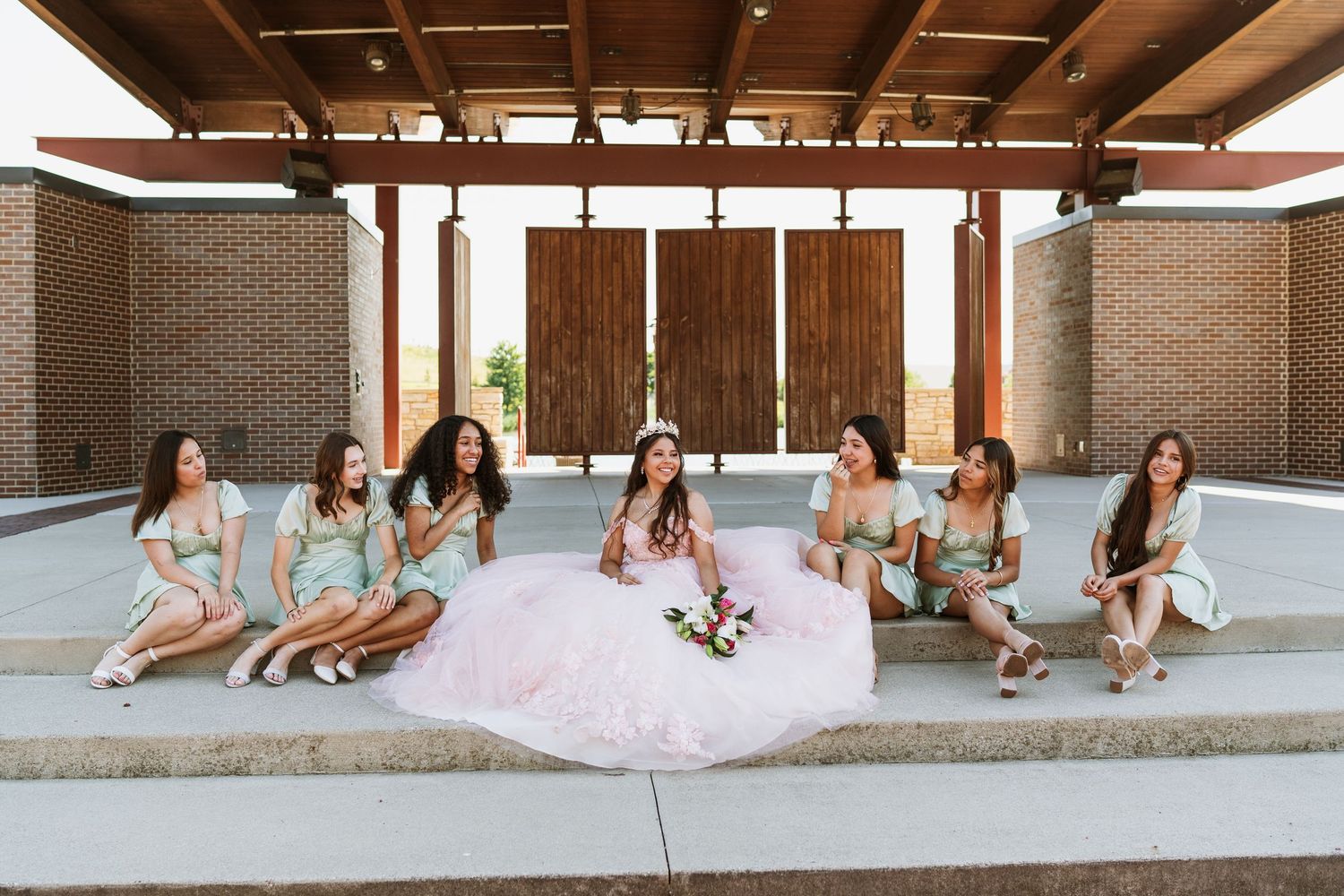 Bridal party relaxing on outdoor steps wearing coordinated outfits for photos.
